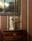 photo of off-white plaster cast sculpture of winged, headless female figure with flowing drapery atop brown antique buffet with wall mirror behind and striped wallpaper behind