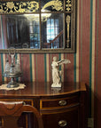 photo of off-white plaster cast sculpture of winged, headless female figure with flowing drapery atop brown antique buffet with wall mirror behind and striped wallpaper behind