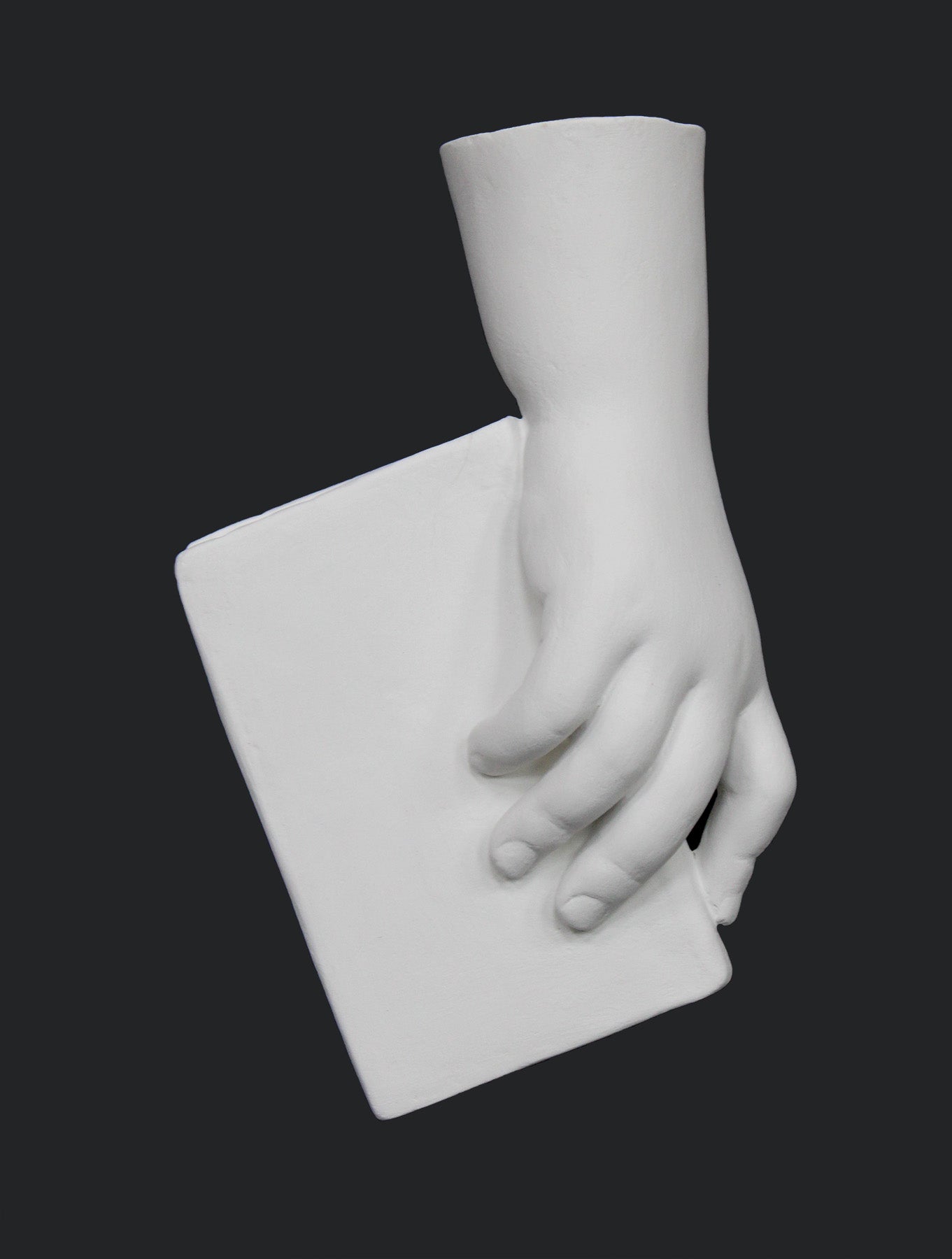 photo of white plaster cast of baby hand holding a book by the spine against gray background