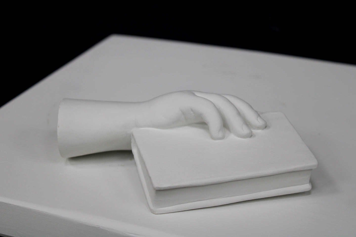 photo of white plaster cast of baby hand holding a book by the spine against white background