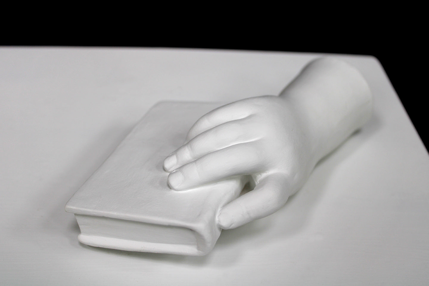 photo of white plaster cast of baby hand holding a book by the spine against white background