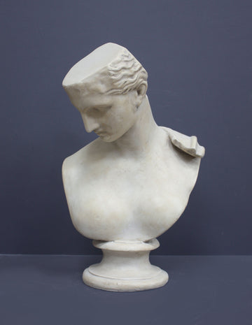 photo of off-white plaster cast sculpture bust of female without top of head and with piece of drapery on socle base on gray background