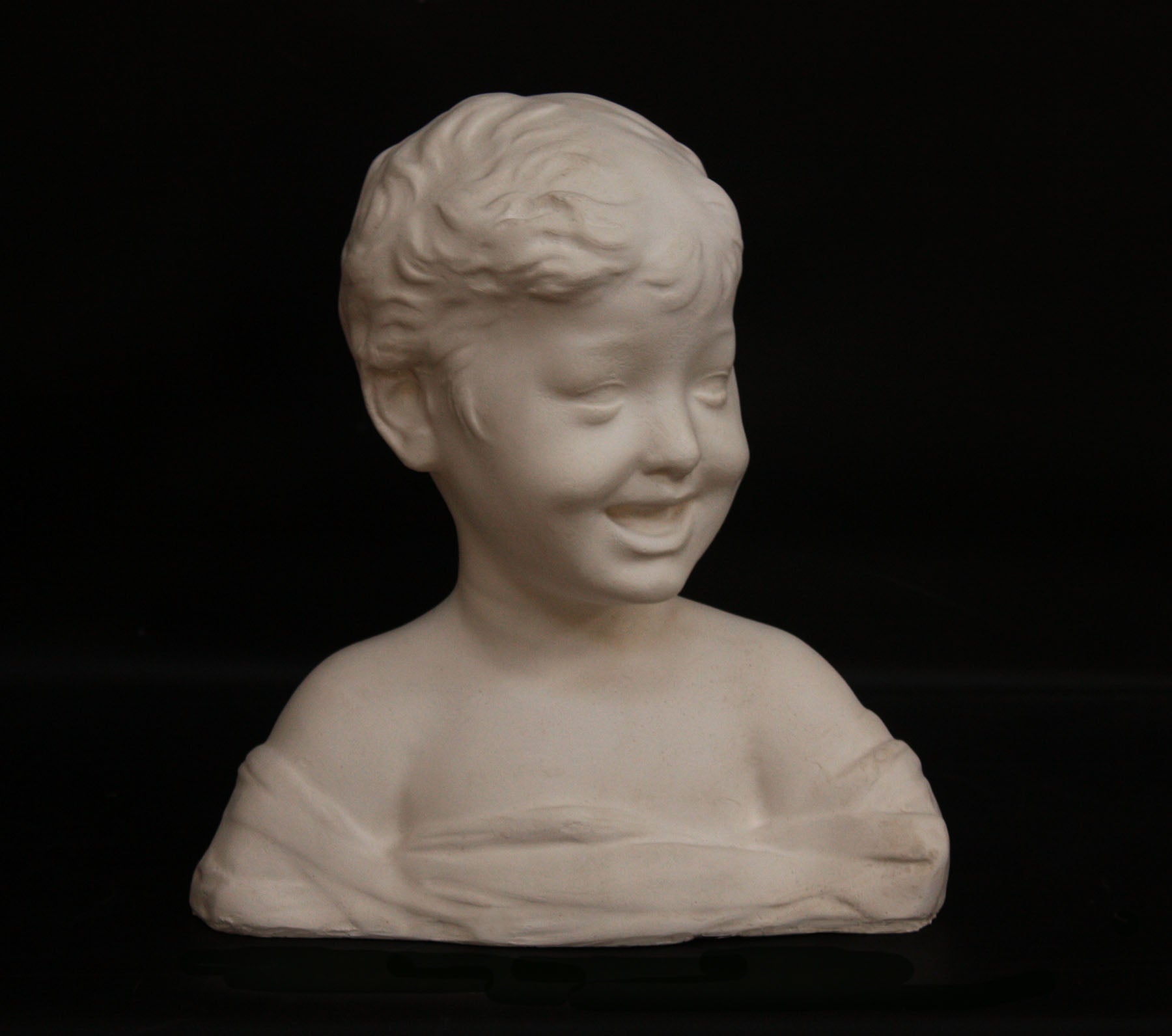 photo of white plaster cast sculpture bust of boy with open mouth, laughing, short hair, and clothes below his shoulders against a black background
