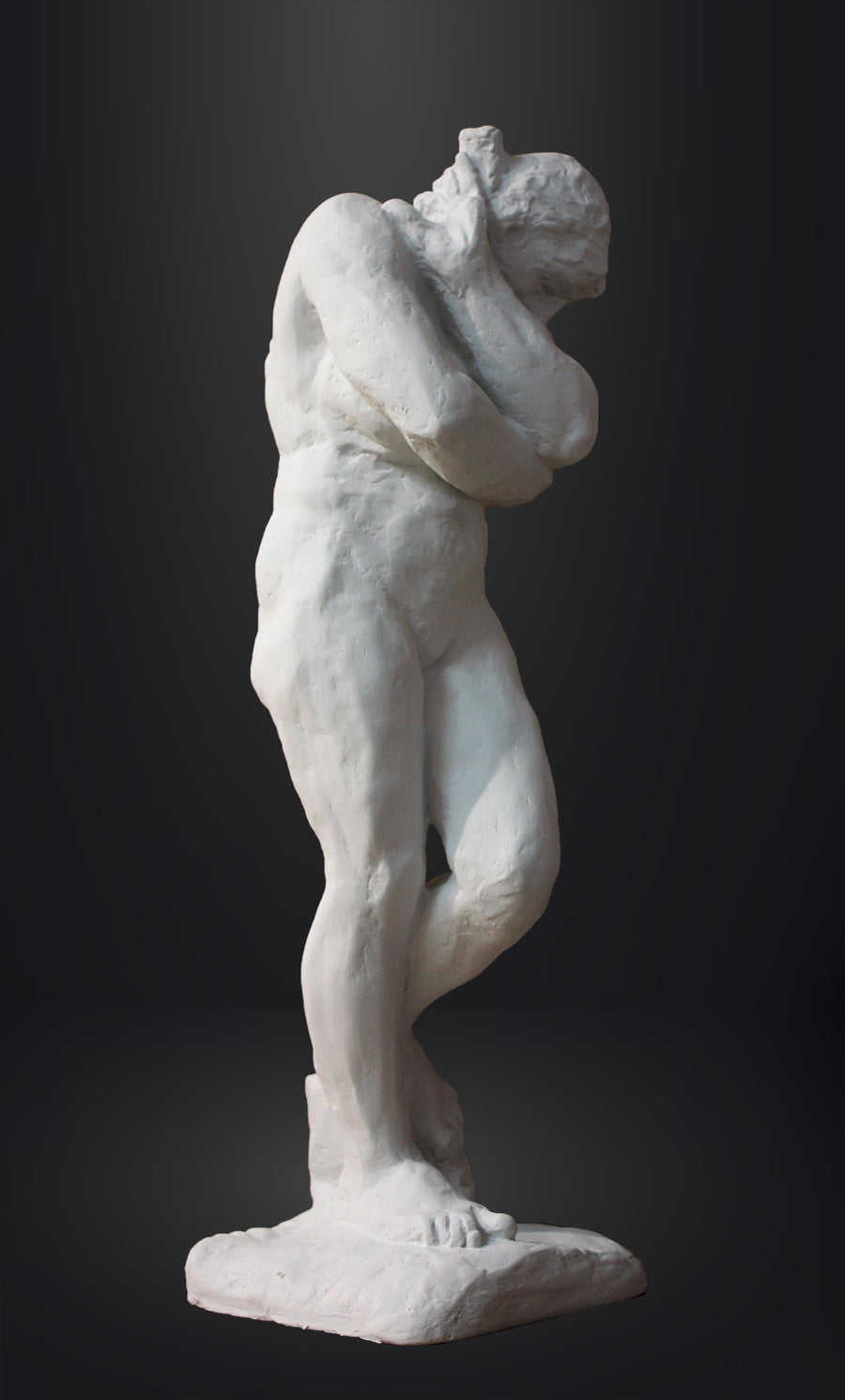 photo of white plaster cast sculpture of nude female figure hugging herself against gray background