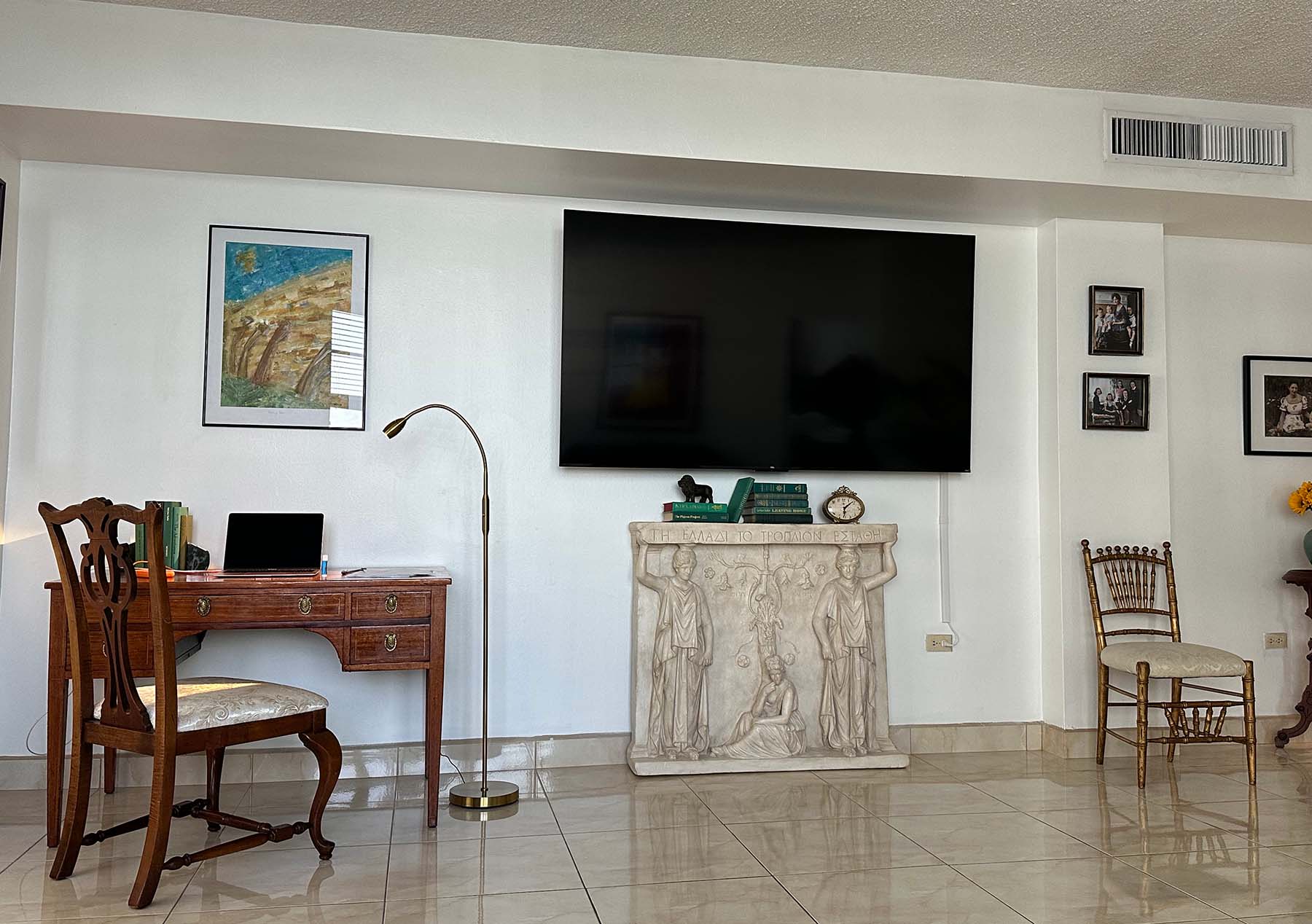 photo of plaster cast of free-standing relief sculpture with three female figures, two of which are caryatides, against a living room wall with a television mounted above it and wooden desk and other decor nearby