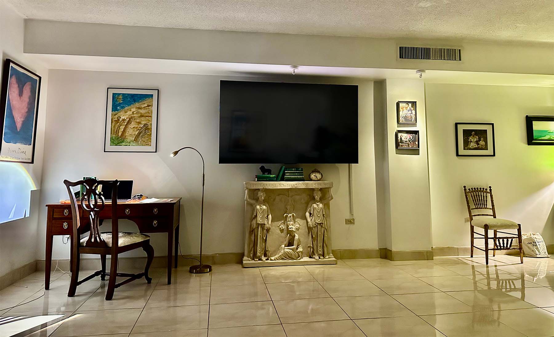 photo of plaster cast of free-standing relief sculpture with three female figures, two of which are caryatides, against a living room wall with a television mounted above it and wooden desk and other decor nearby