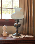 photo of white plaster cast head of male on brown nightstand beside silver lamp with milk glass in front of window