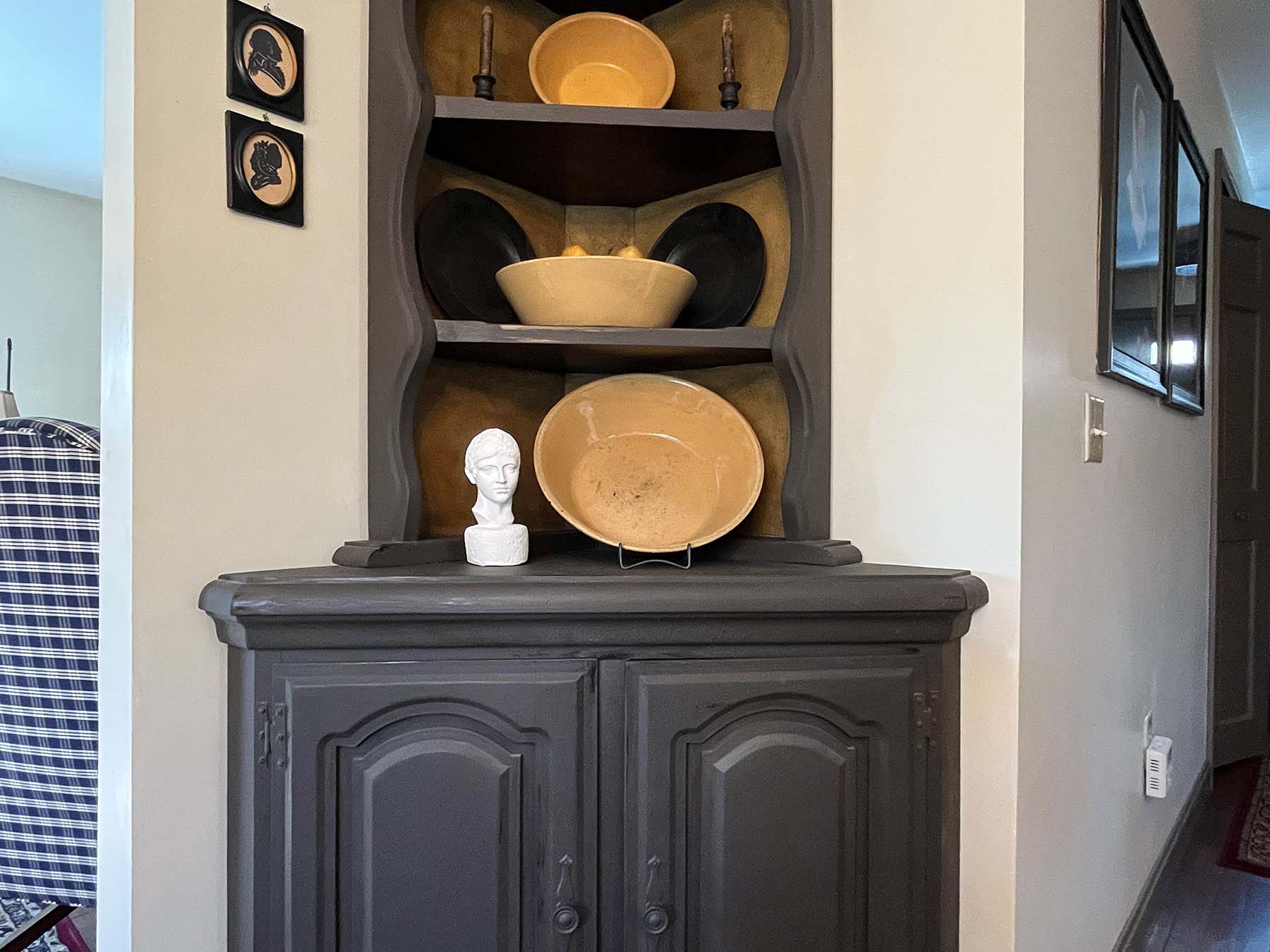 photo of white plaster cast head of male on tall country black cabinet filled with cream and black dishes and bowls