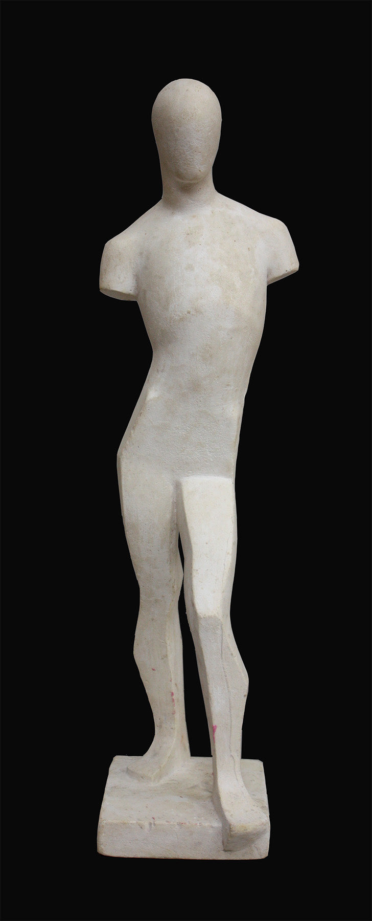 photo of white plaster cast sculpture reproduction of human form in blocked manner standing in contrapposto against black background