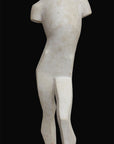 photo of white plaster cast sculpture reproduction of human form in blocked manner standing in contrapposto against black background