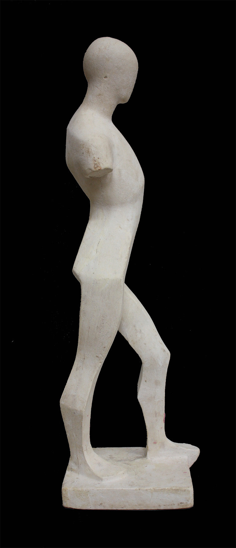 photo of white plaster cast sculpture reproduction of human form in blocked manner standing in contrapposto against black background