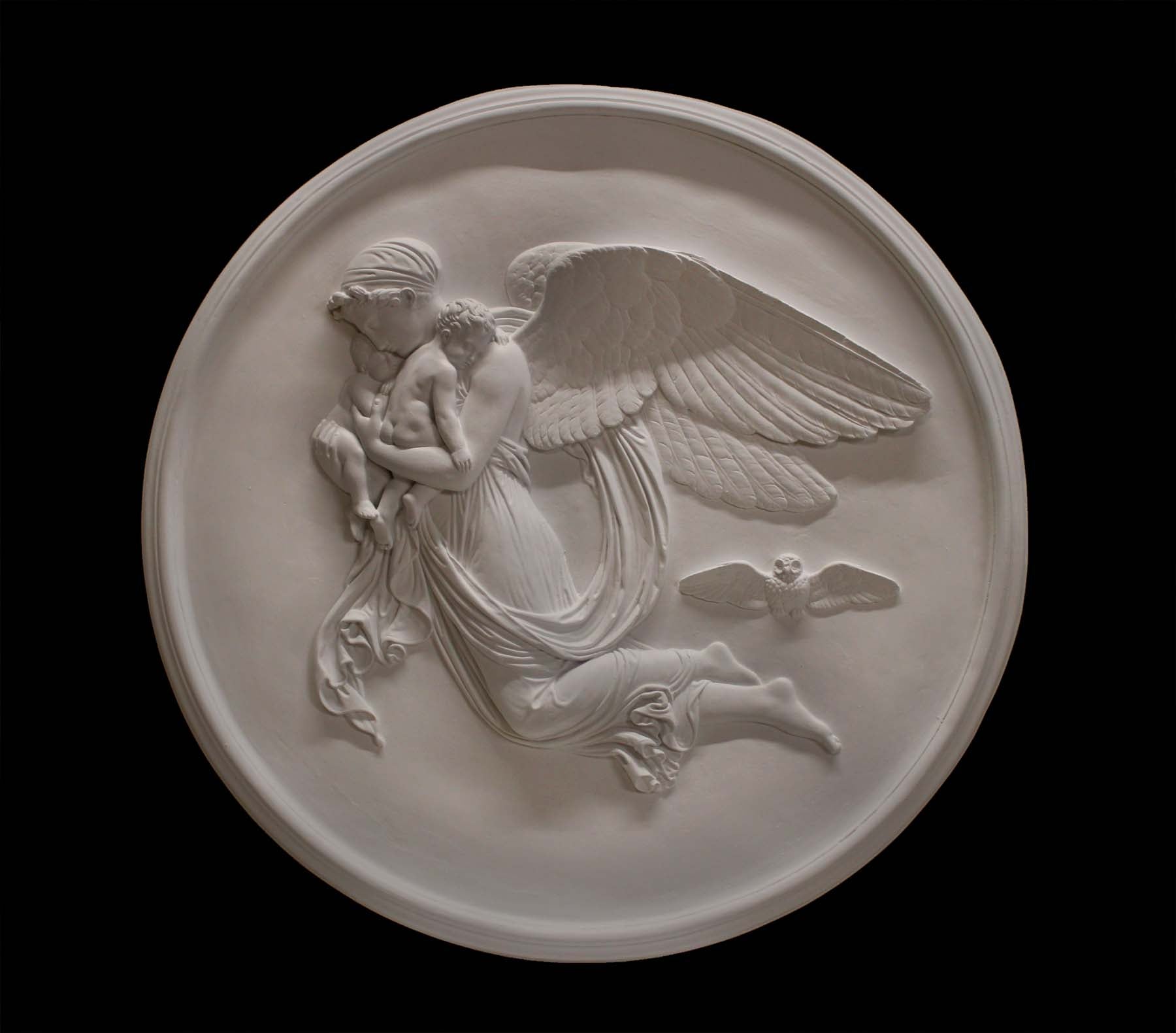photo of plaster cast relief of woman with wings flying with two children nestled against her and an owl flying on a dark background