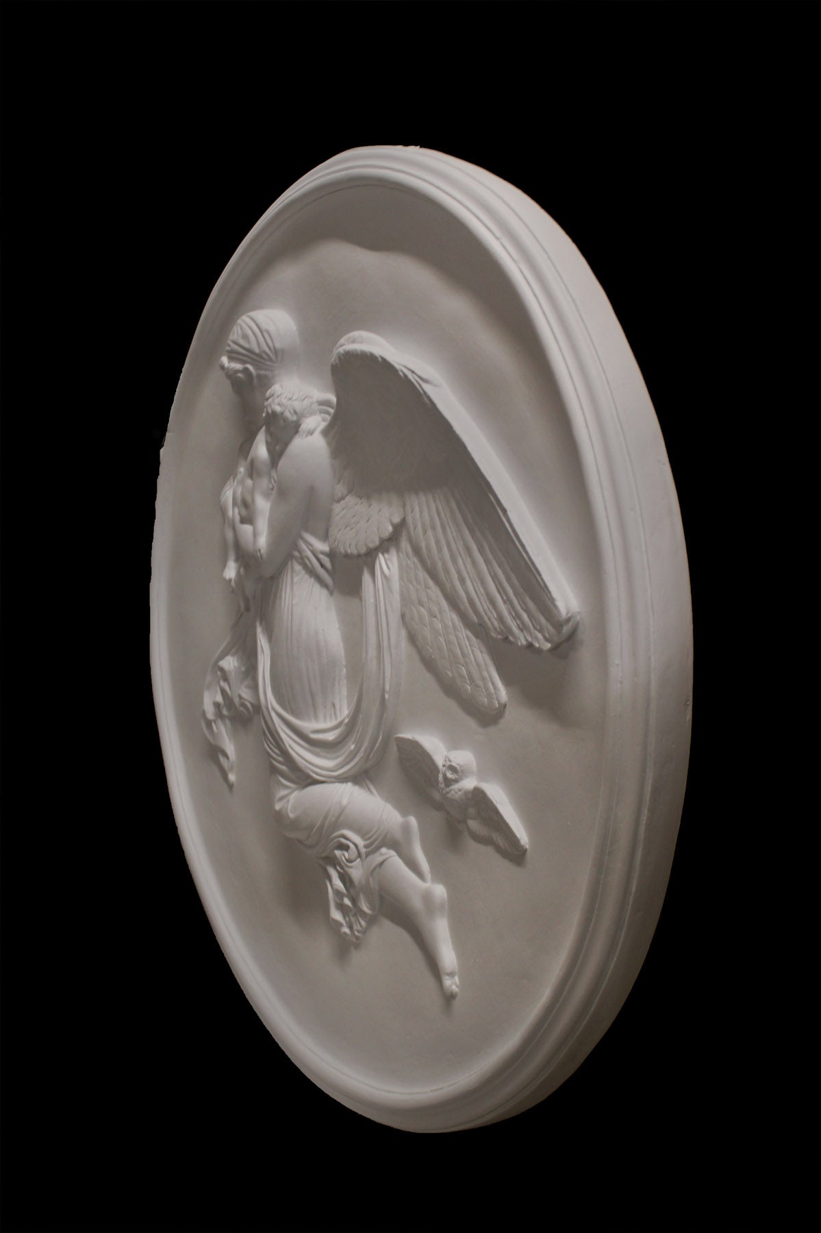 photo of plaster cast relief of woman with wings flying with two children nestled against her and an owl flying on a dark background