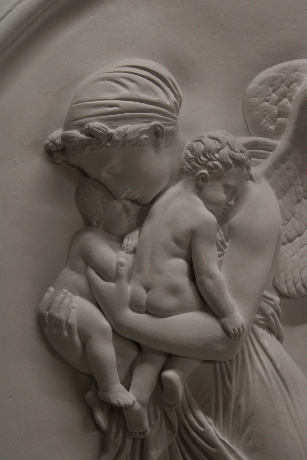 detail photo of plaster cast relief of woman with wings flying with two children nestled against her and an owl flying on a dark background