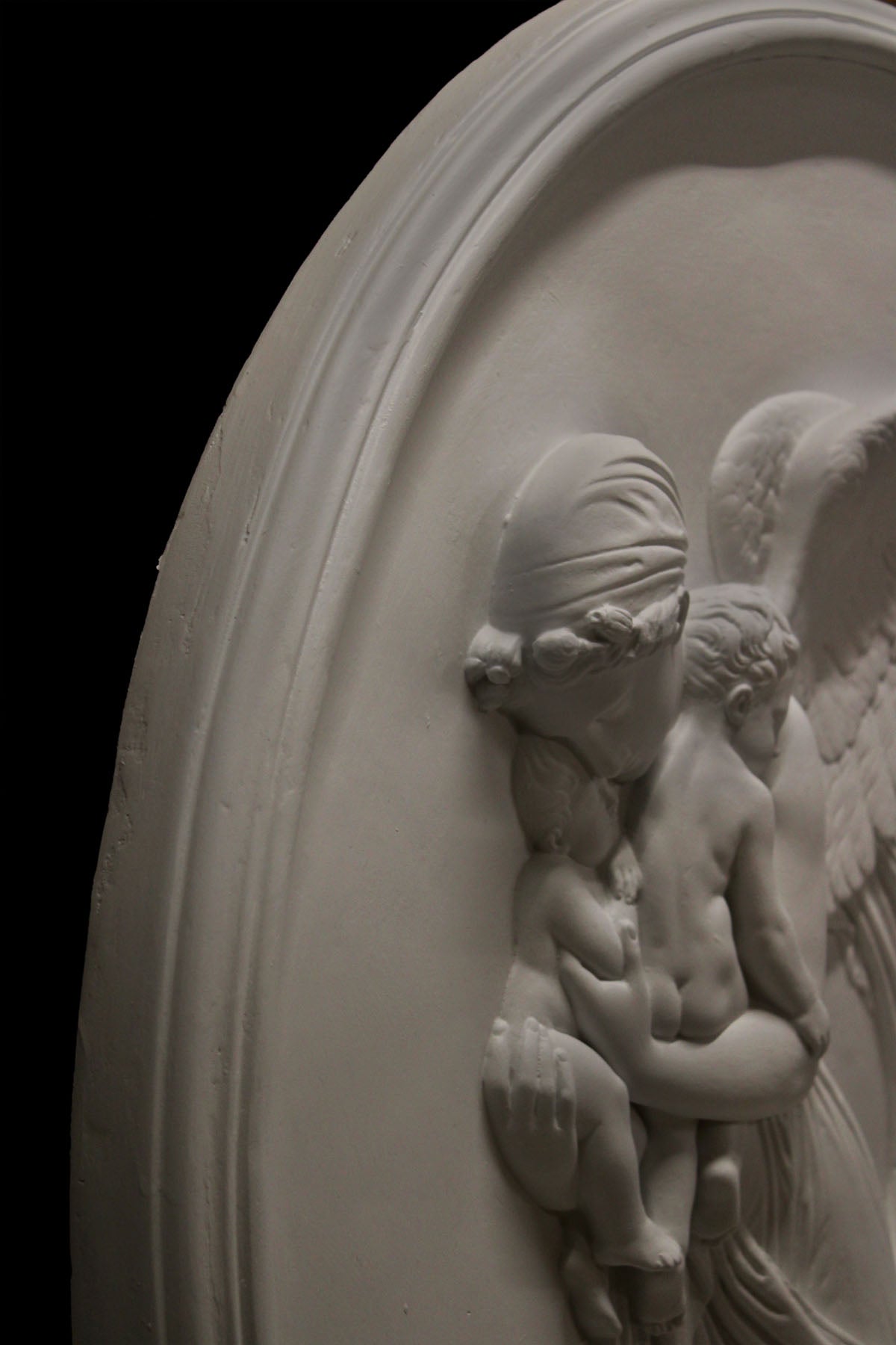 detail photo of plaster cast relief of woman with wings flying with two children nestled against her and an owl flying on a dark background
