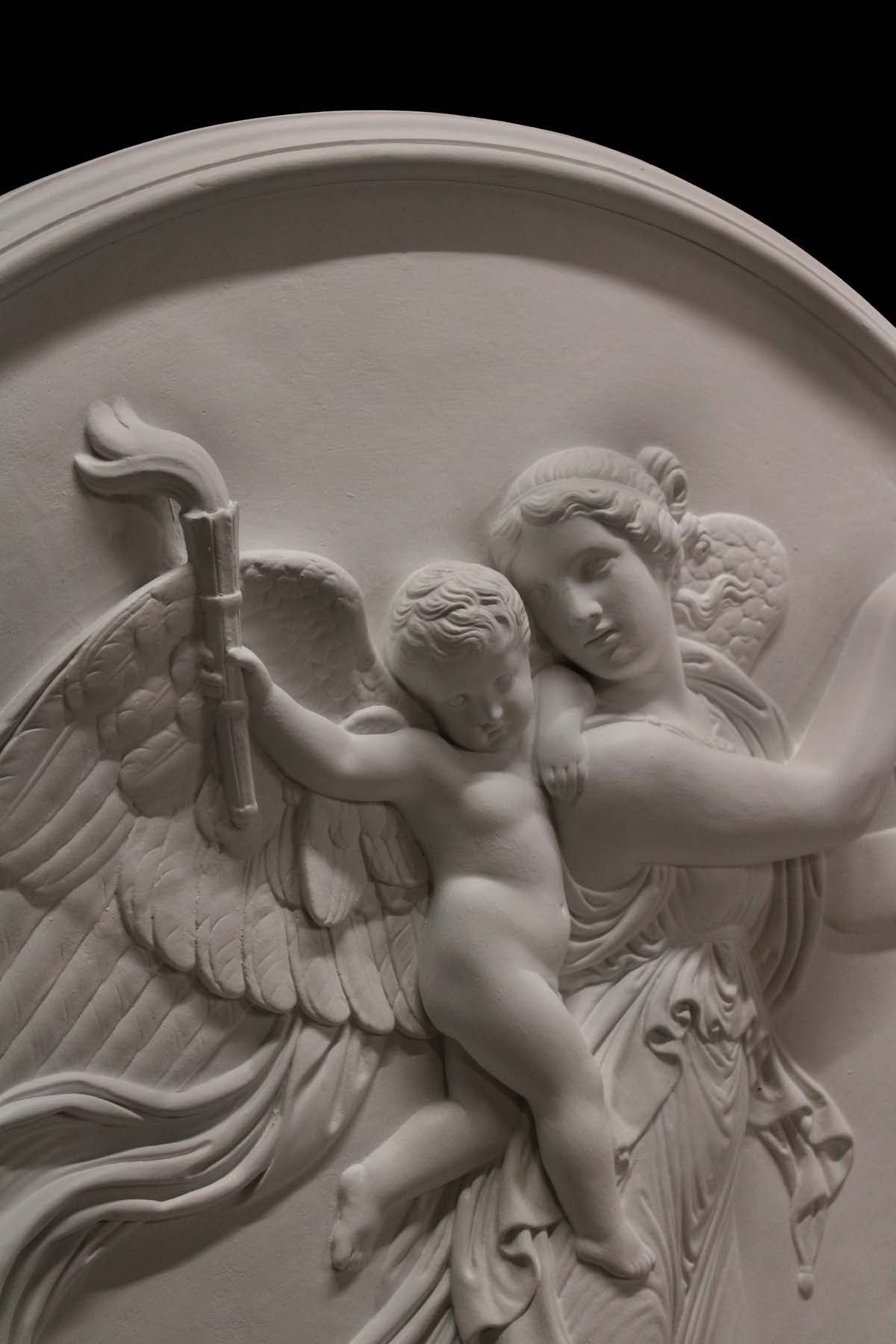  detail photo of plaster cast relief of female with wings flying and a cherub on her back on black background