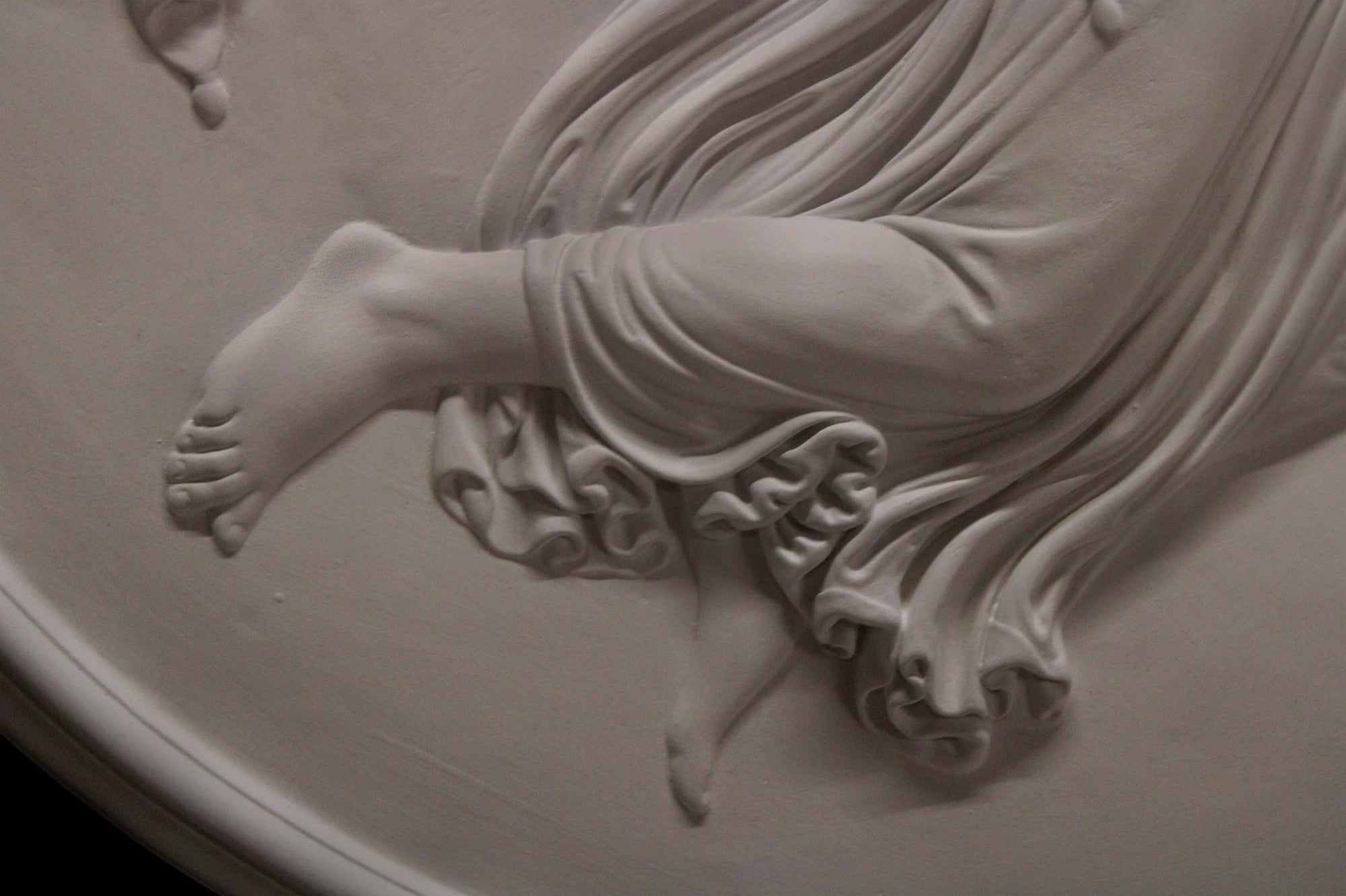 detail  photo of plaster cast relief of female with wings flying and a cherub on her back on black background