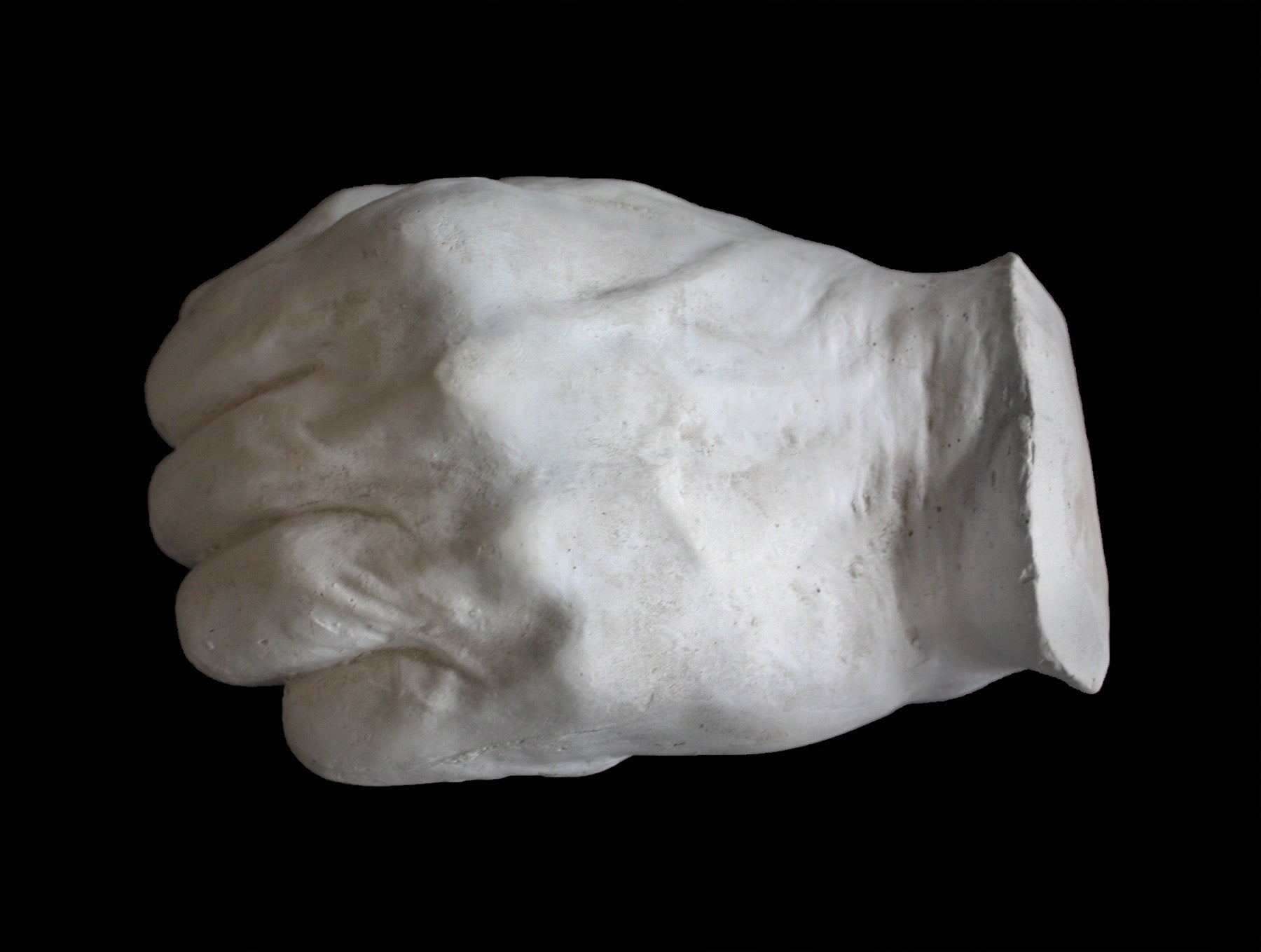 Photo of white plaster cast of a life cast of a clenched fisted hand on a black background