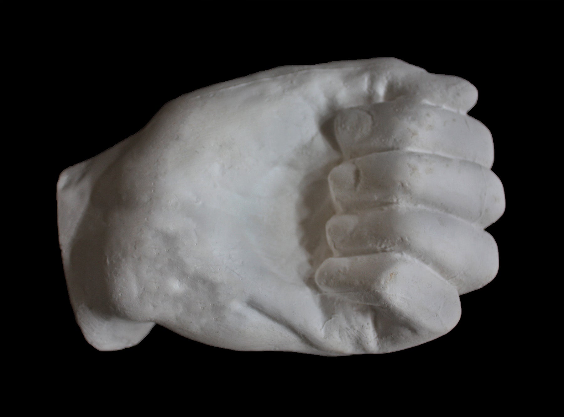 Photo of white plaster cast of a life cast of a clenched fisted hand on a black background