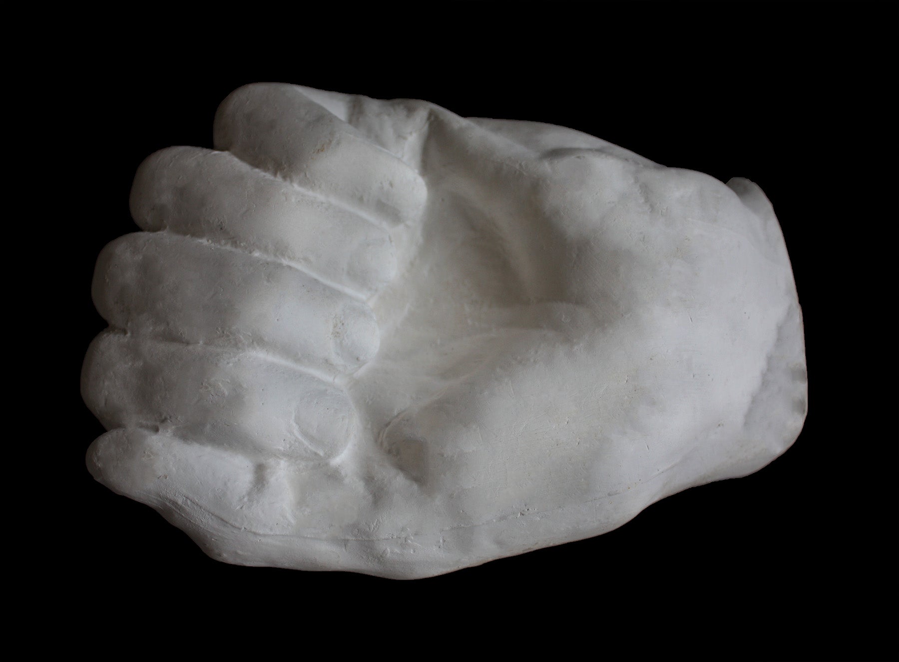 Photo of white plaster cast of a life cast of a clenched fisted hand on a black background