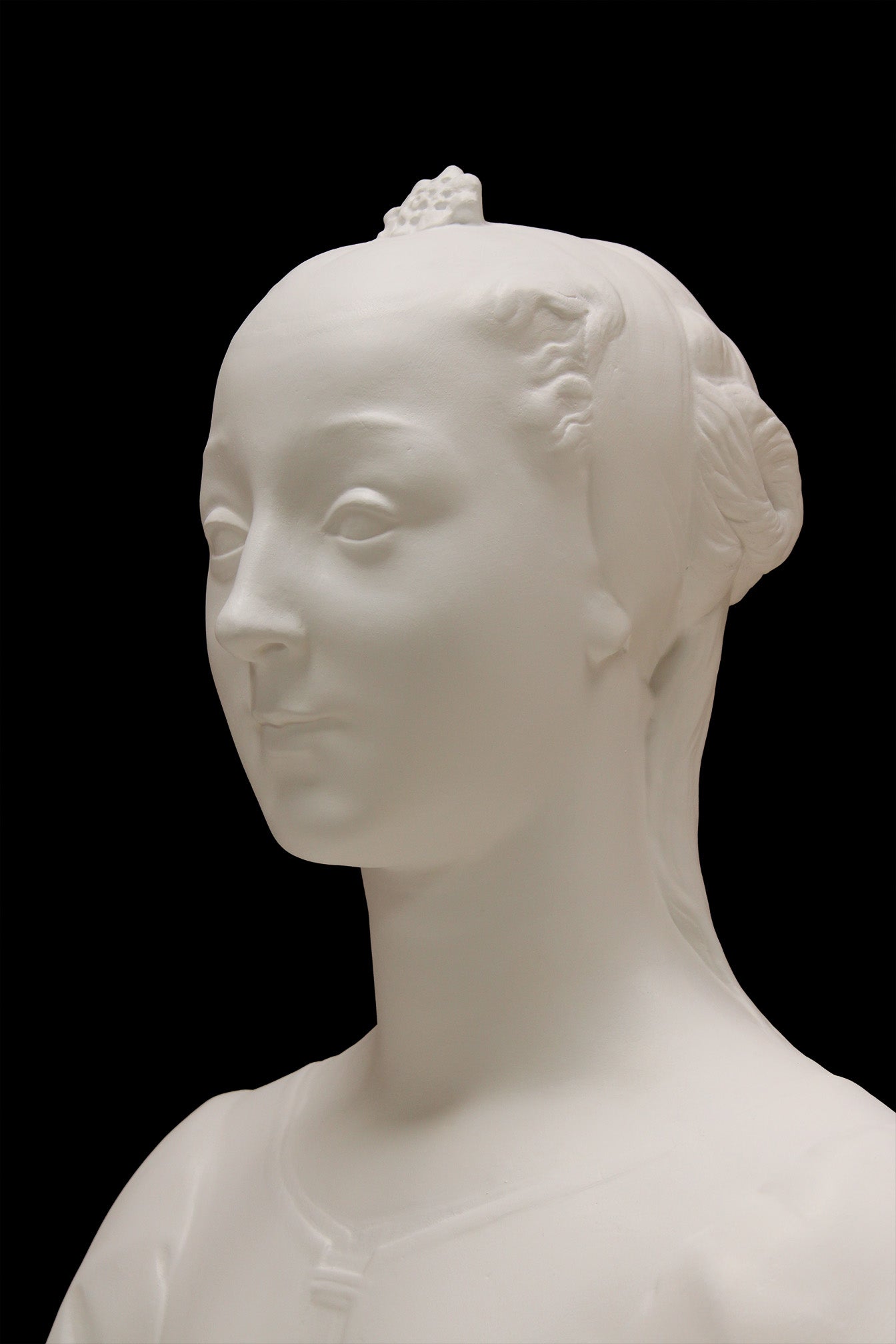 photo of white plaster cast of female bust with up-do and dress against black background