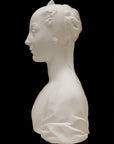 photo of white plaster cast of female bust with up-do and dress against black background