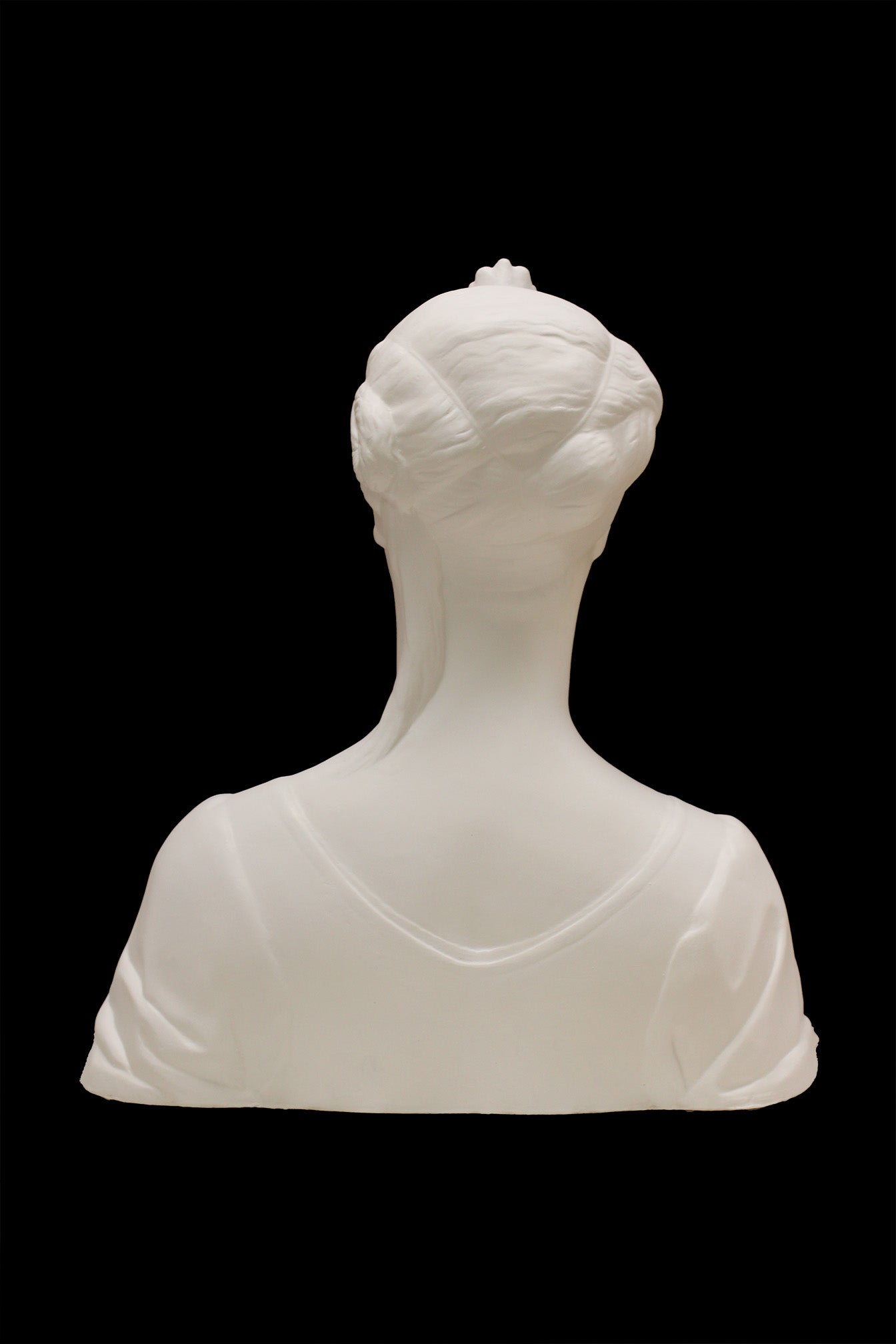 photo of white plaster cast of female bust with up-do and dress against black background