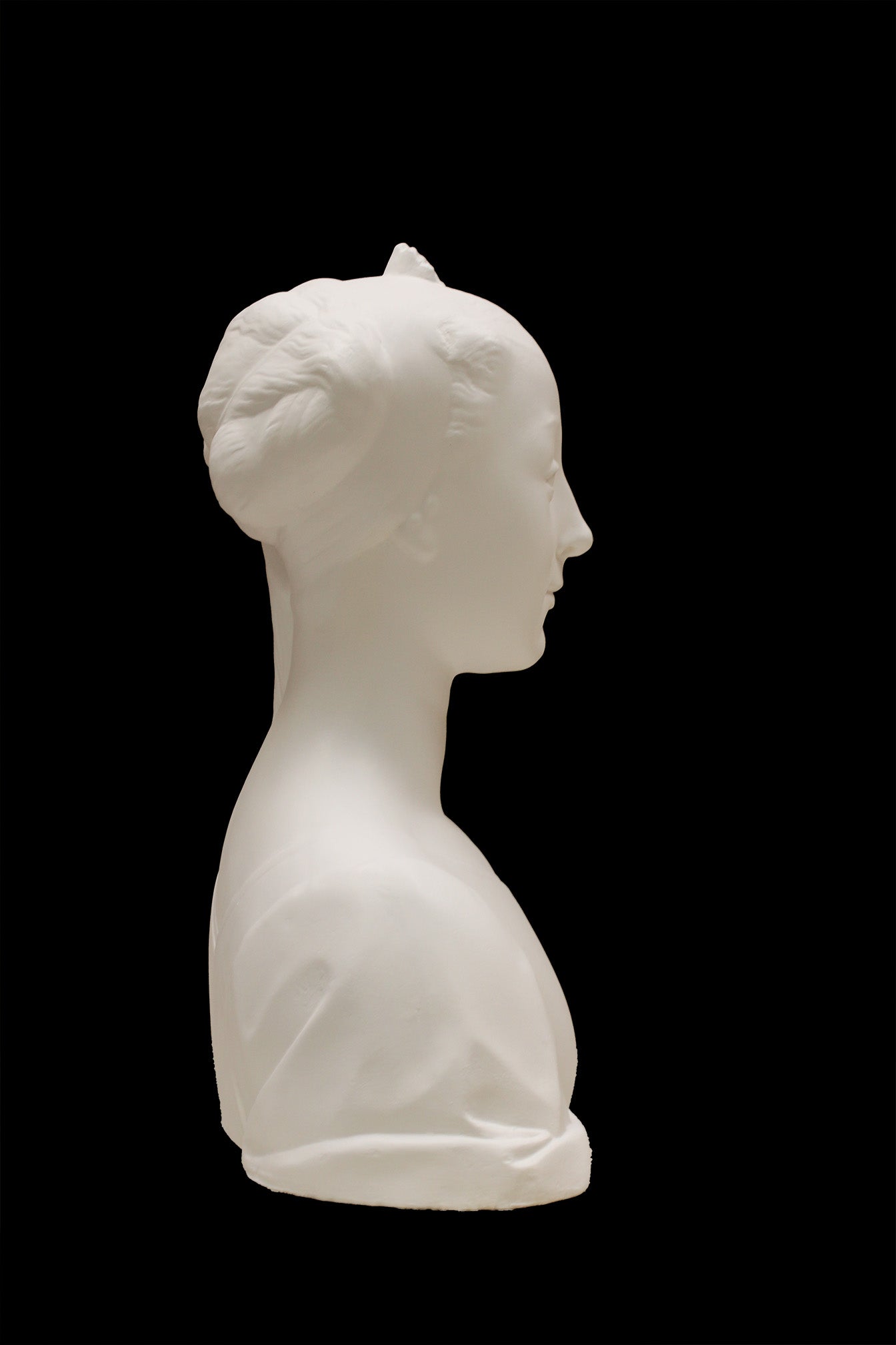 photo of white plaster cast of female bust with up-do and dress against black background