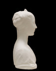 photo of white plaster cast of female bust with up-do and dress against black background