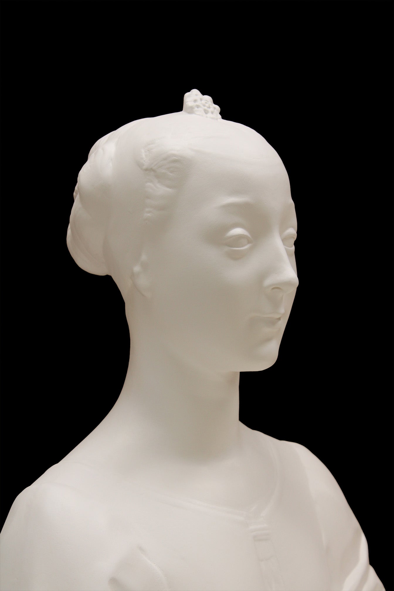 photo of white plaster cast of female bust with up-do and dress against black background