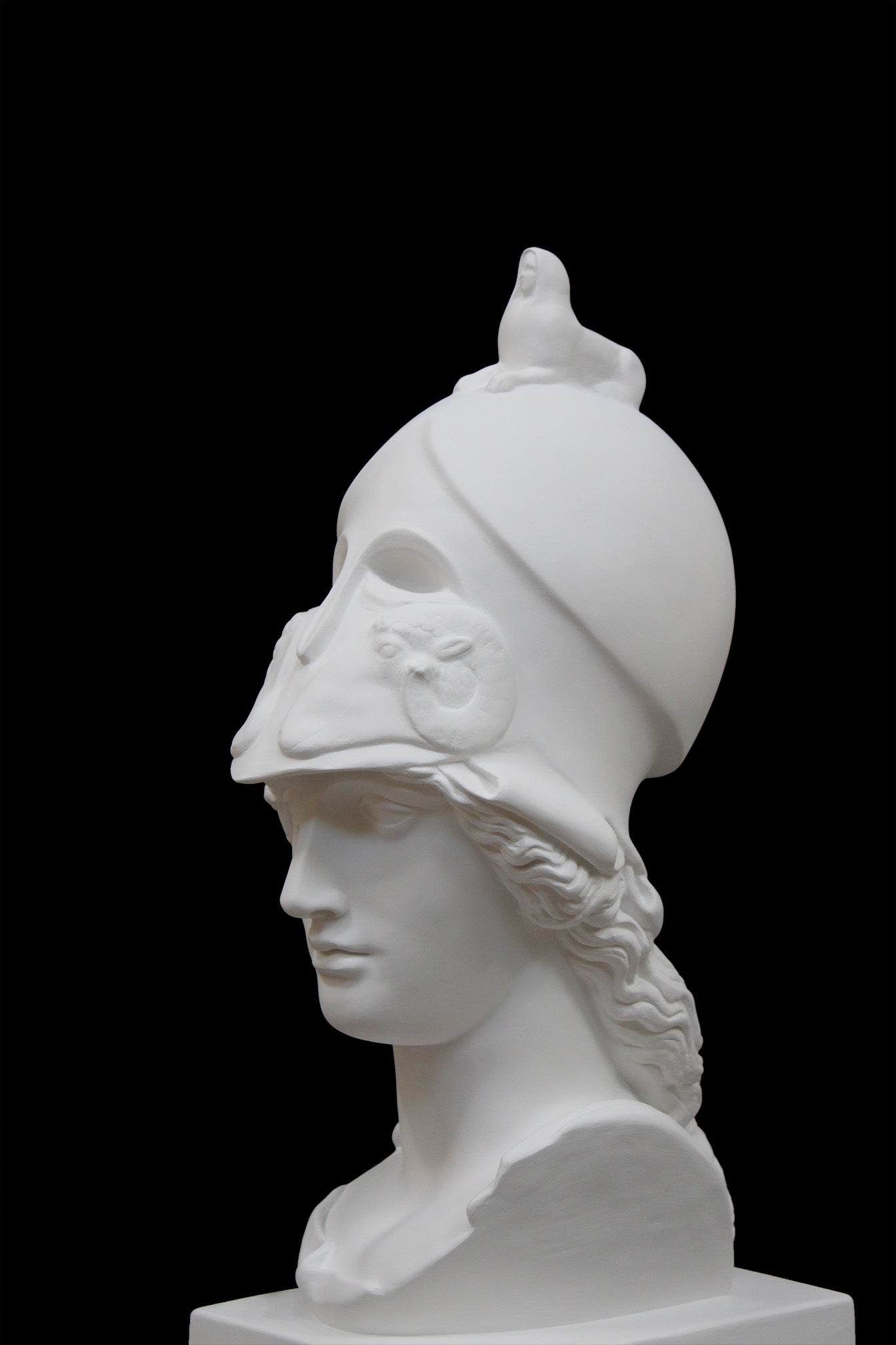 photo of plaster cast sculpture bust of female head, namely the goddess Athena, with a helmet on a black background