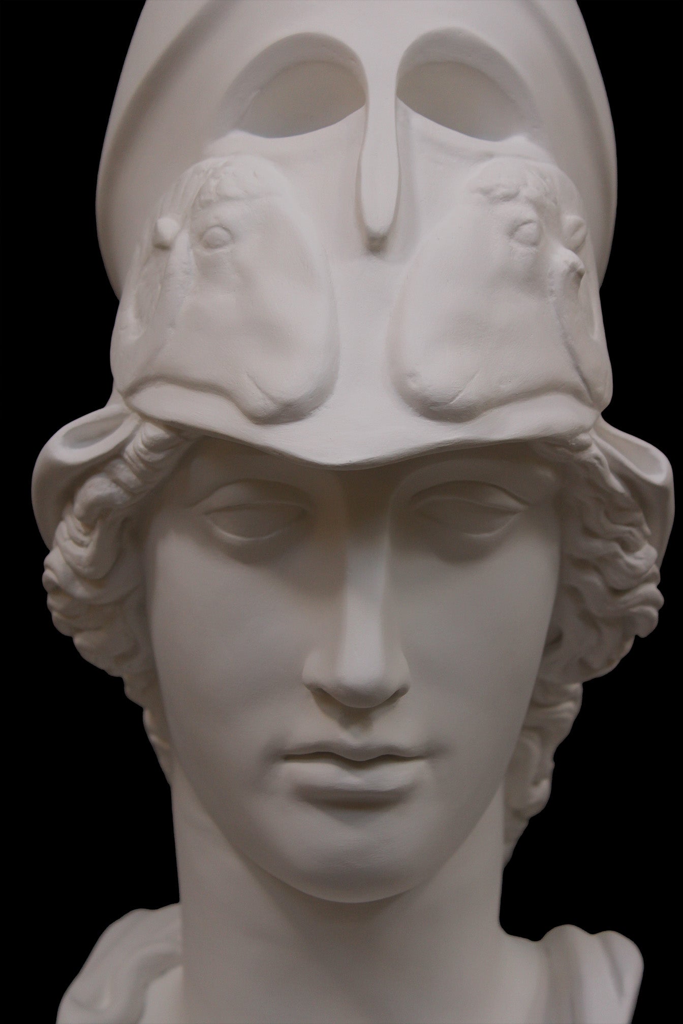 photo of plaster cast sculpture bust of female head, namely the goddess Athena, with a helmet on a black background