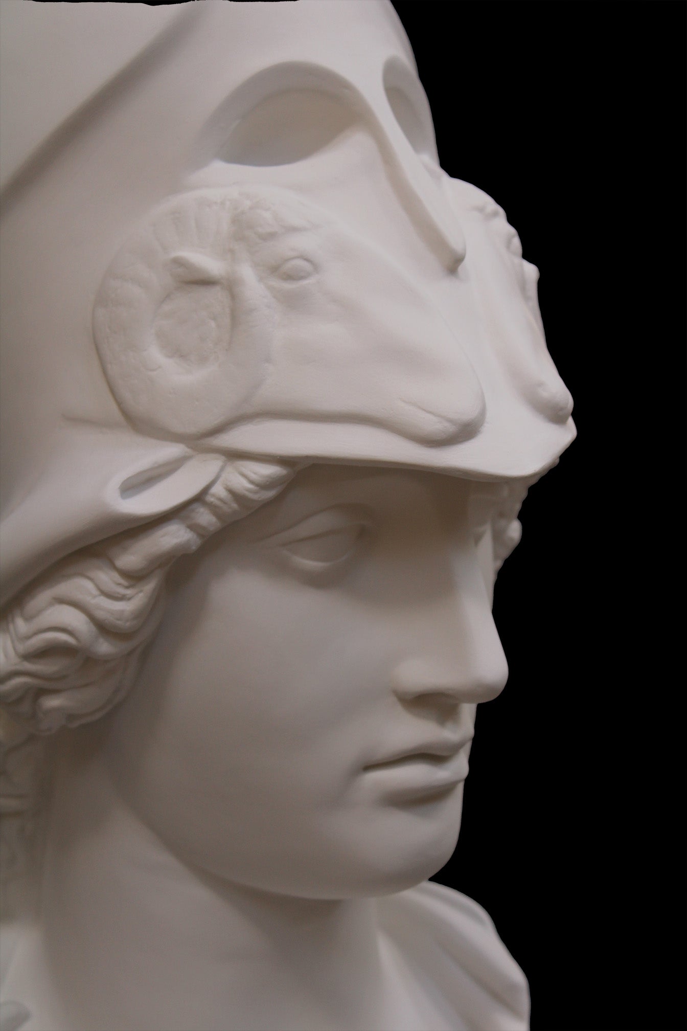 photo of plaster cast sculpture bust of female head, namely the goddess Athena, with a helmet on a black background