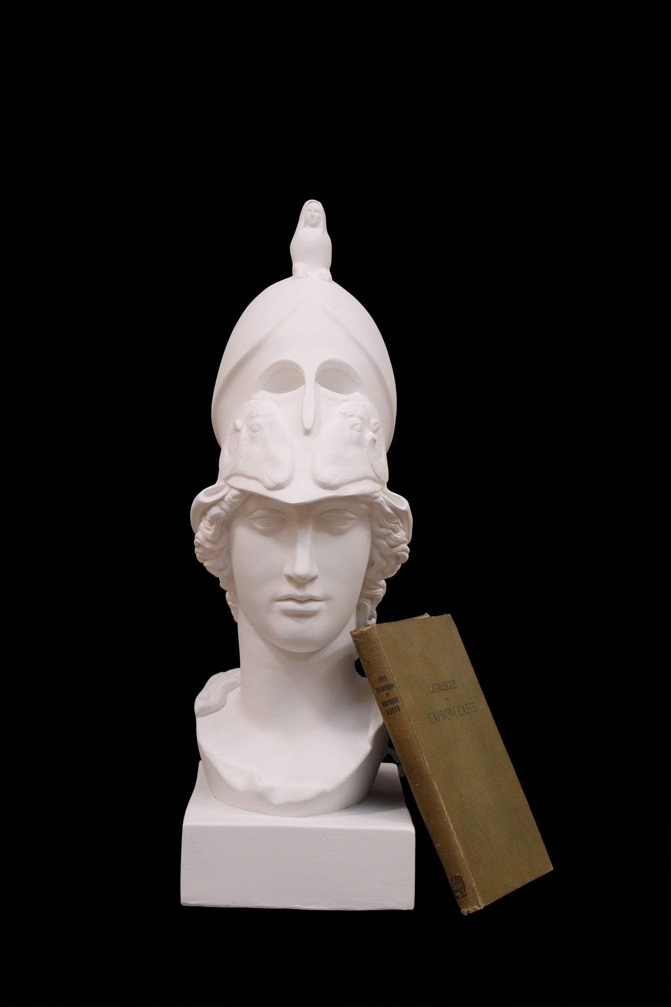 photo of plaster cast sculpture bust of female head, namely the goddess Athena, with a helmet on a black background