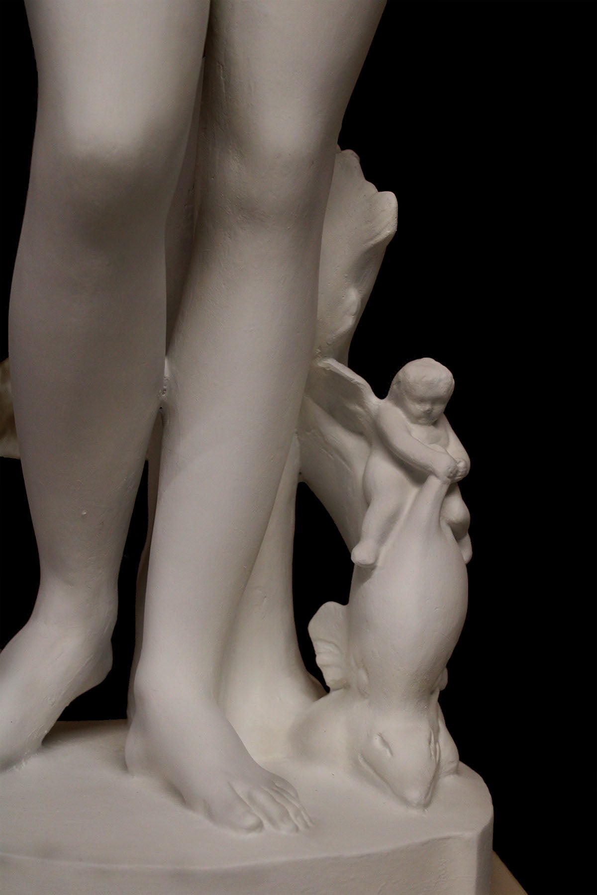 detail photo of plaster cast sculpture of Venus standing nude with two putti riding a dolphin at her feet on black background