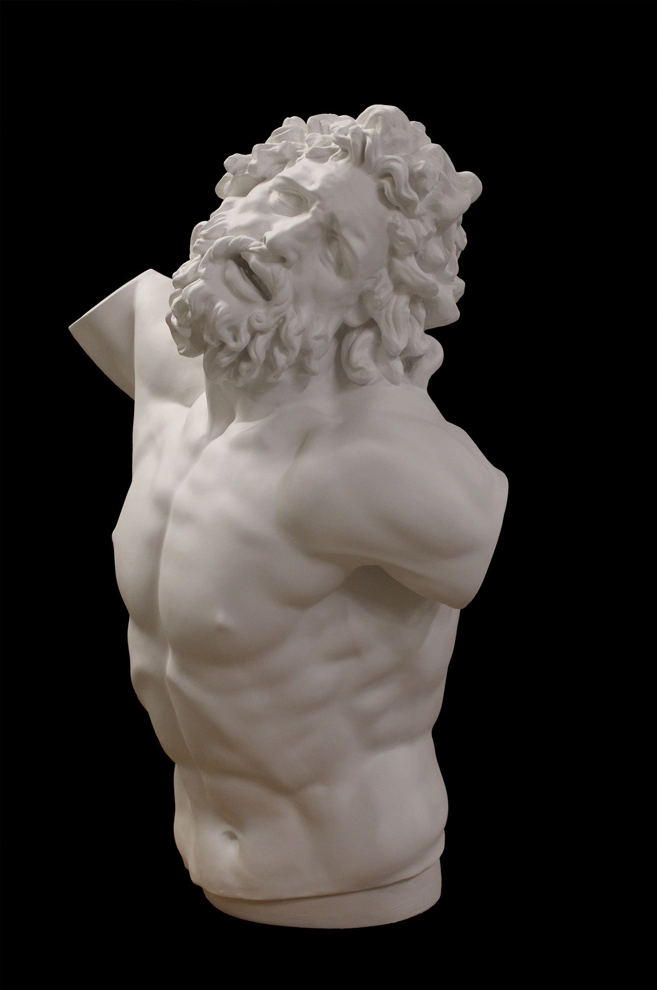 photo with black background of plaster cast of sculpted male torso and head with curly hair and beard, namely Laocoon
