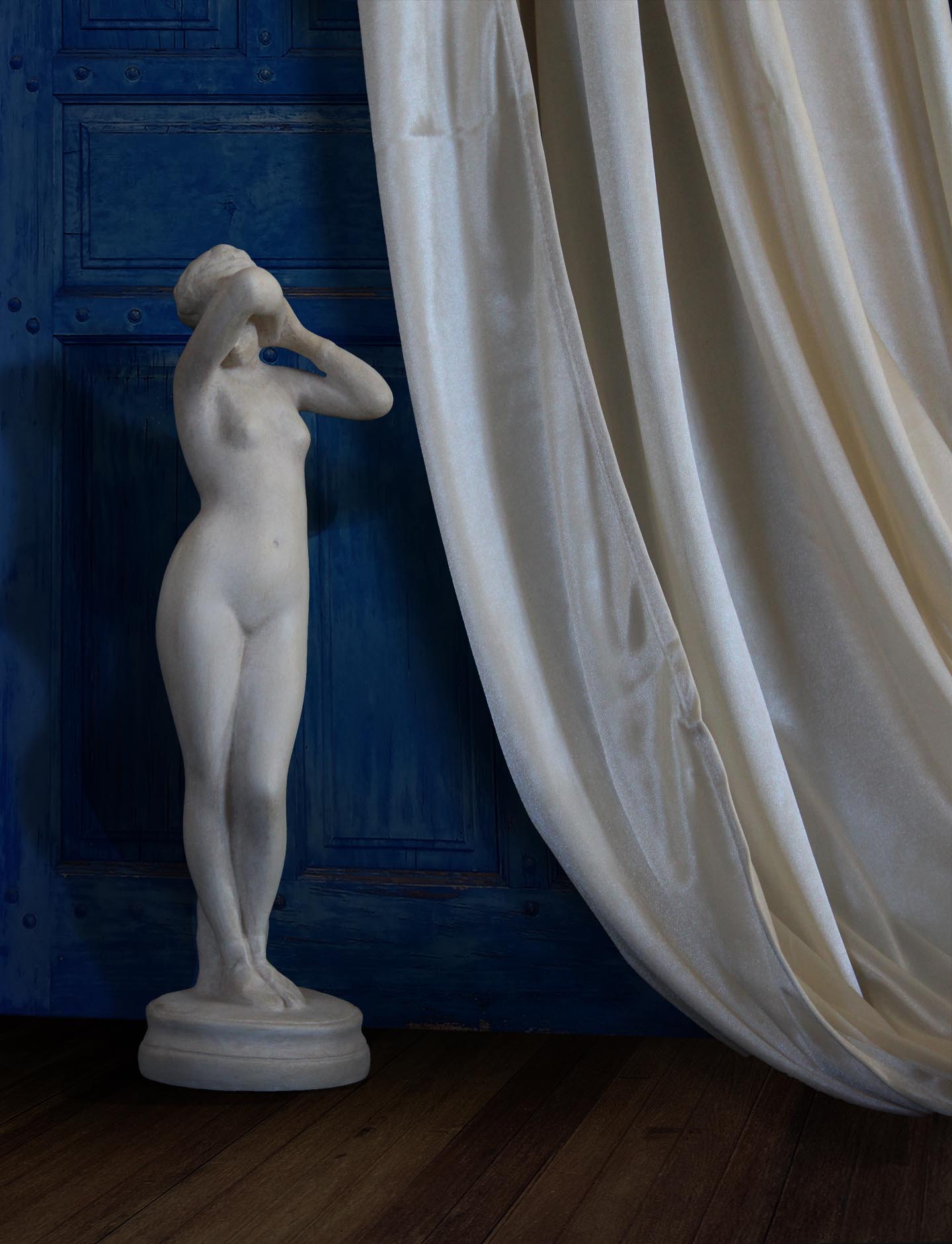image of a plaster statue of a nude female figure, namely Phryne,  next to a cream-colored curtain on a detailed background of a blue wooden wall/door and brown wood floor