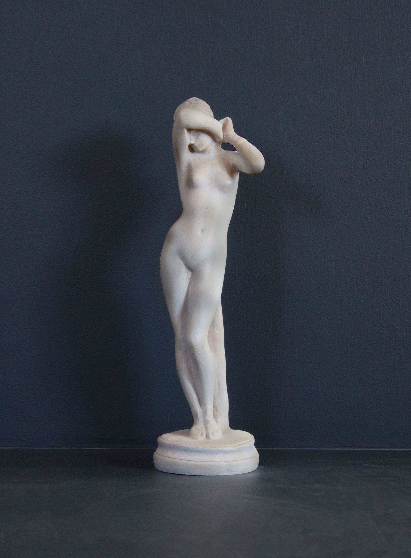 image of a plaster statue of a nude female figure, namely Phryne, on a gray background