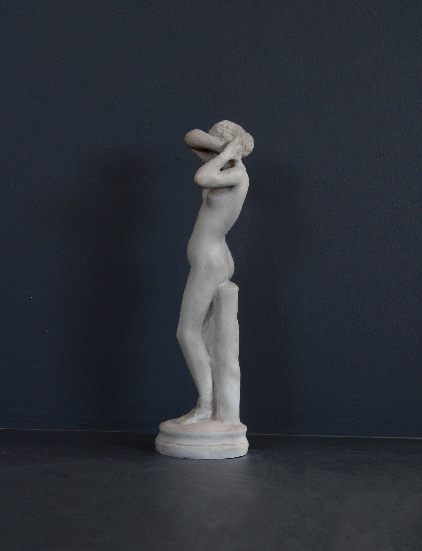 image of a plaster statue of a nude female figure, namely Phryne, on a gray background