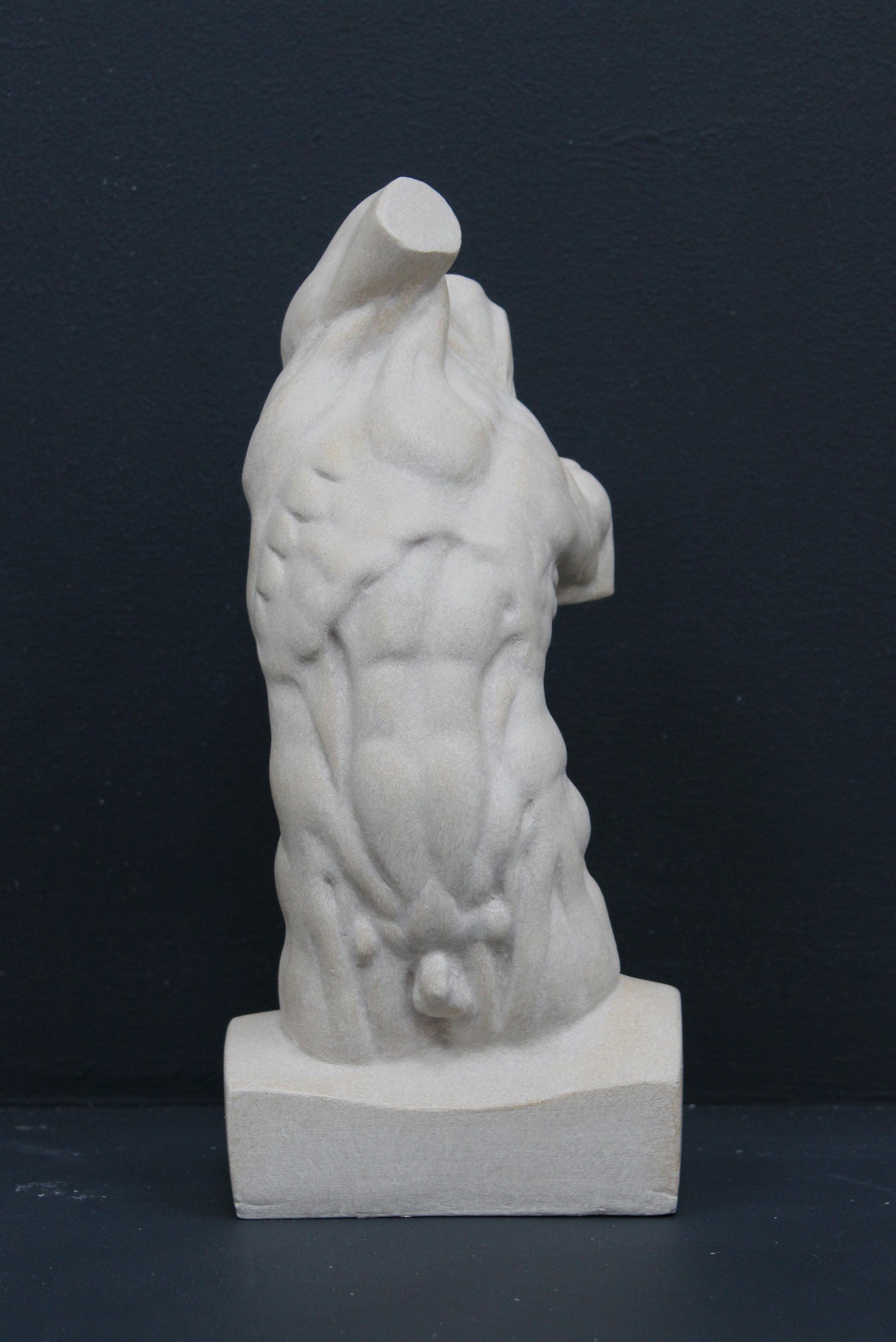 Photo of plaster cast sculpture of flayed male torso and a sculpting tool on a gray surface in front of a black background
