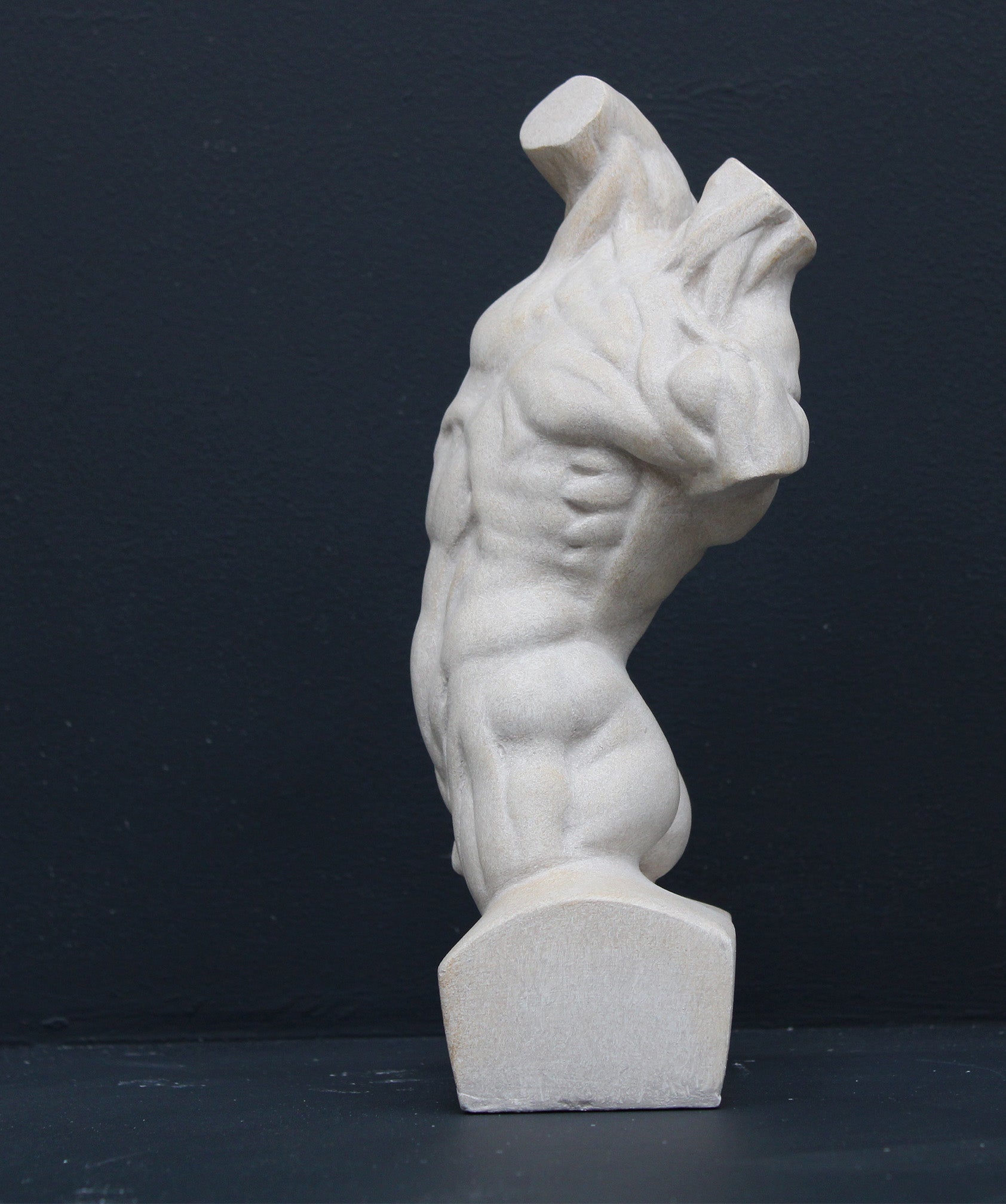 Photo of plaster cast sculpture of flayed male torso and a sculpting tool on a gray surface in front of a black background