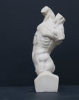 Photo of plaster cast sculpture of flayed male torso and a sculpting tool on a gray surface in front of a black background