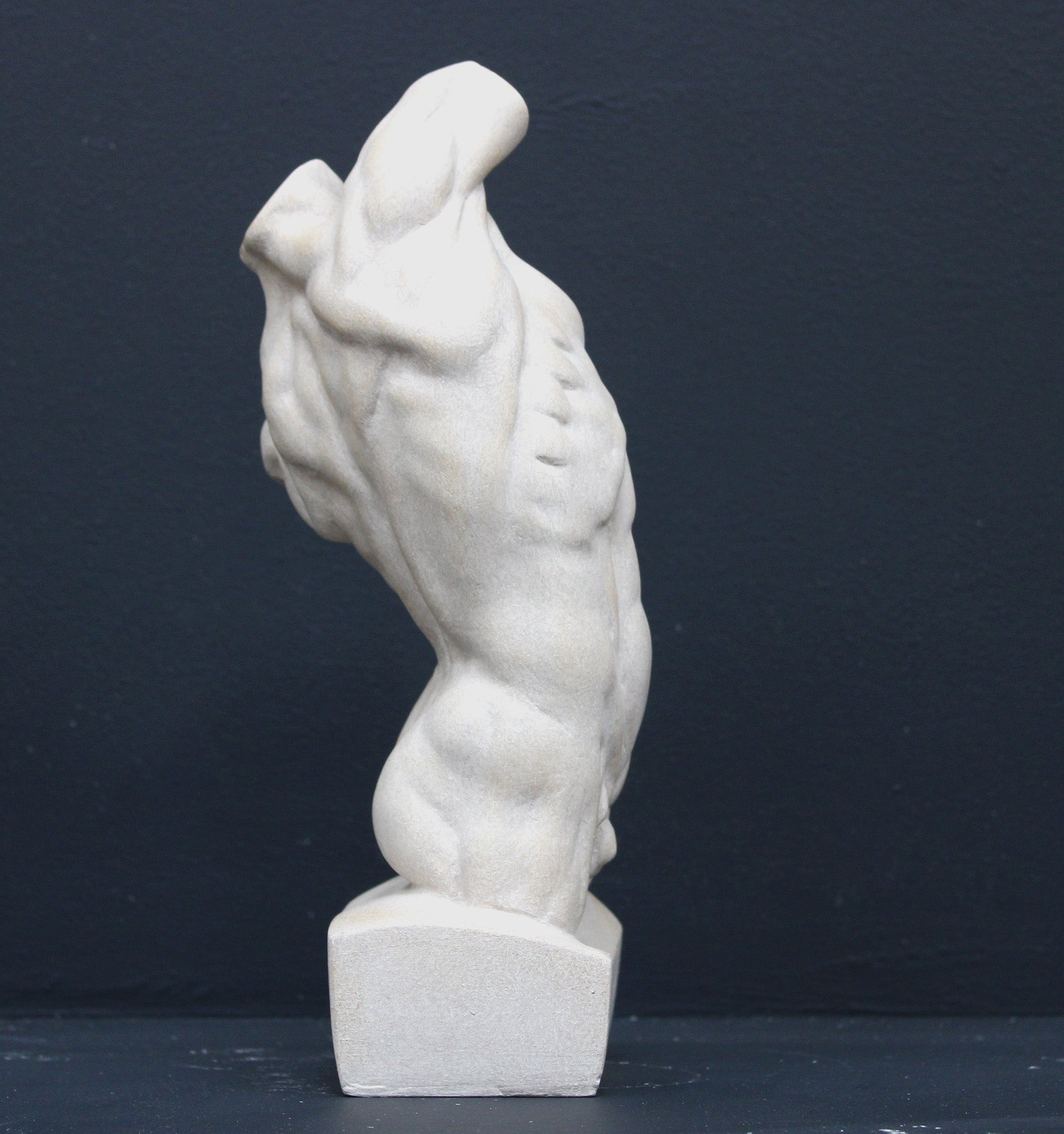 Photo of plaster cast sculpture of flayed male torso and a sculpting tool on a gray surface in front of a black background