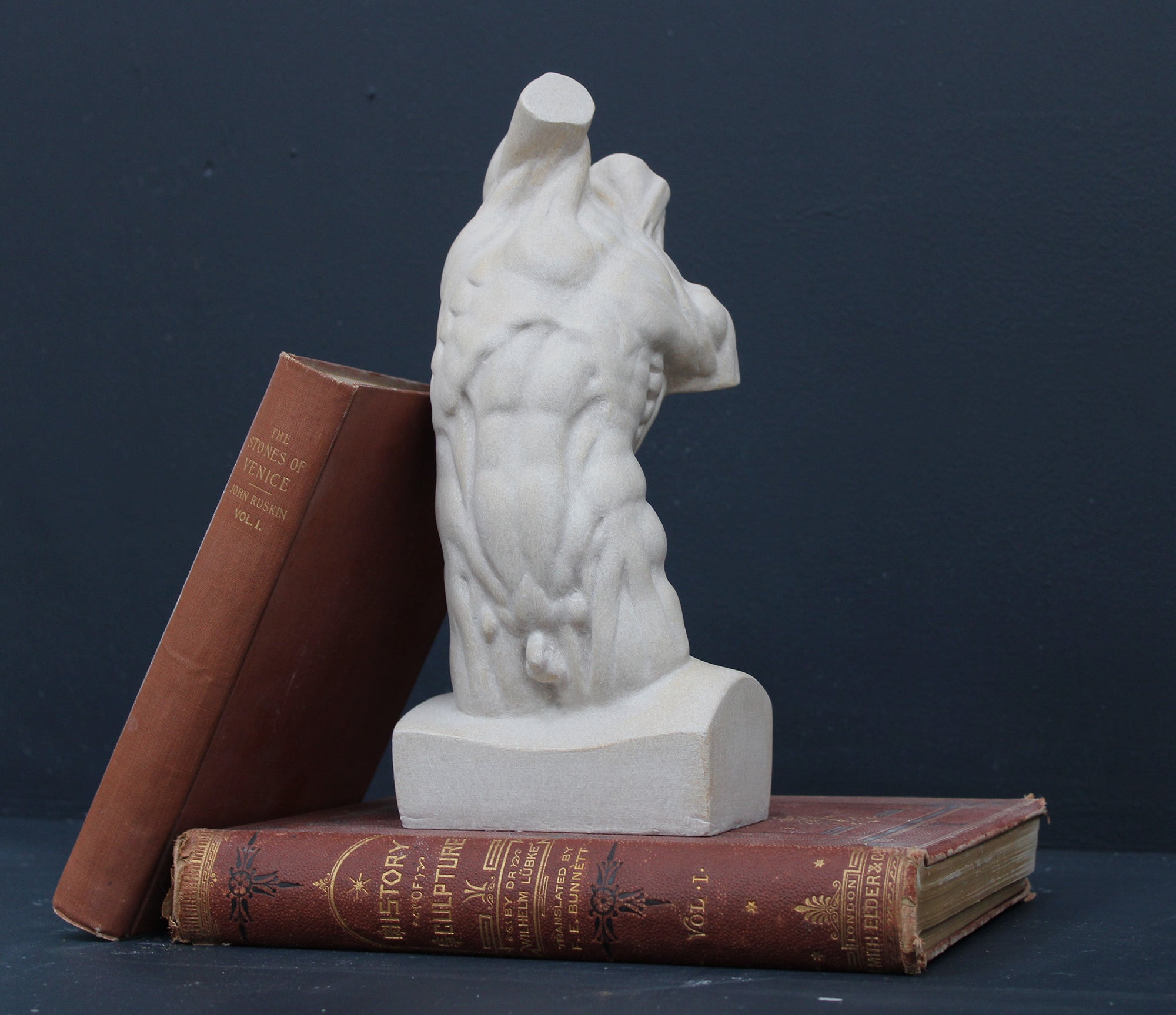 Photo of plaster cast sculpture of flayed male torso and a sculpting tool on a gray surface in front of a black background