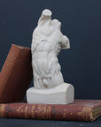 Photo of plaster cast sculpture of flayed male torso and a sculpting tool on a gray surface in front of a black background