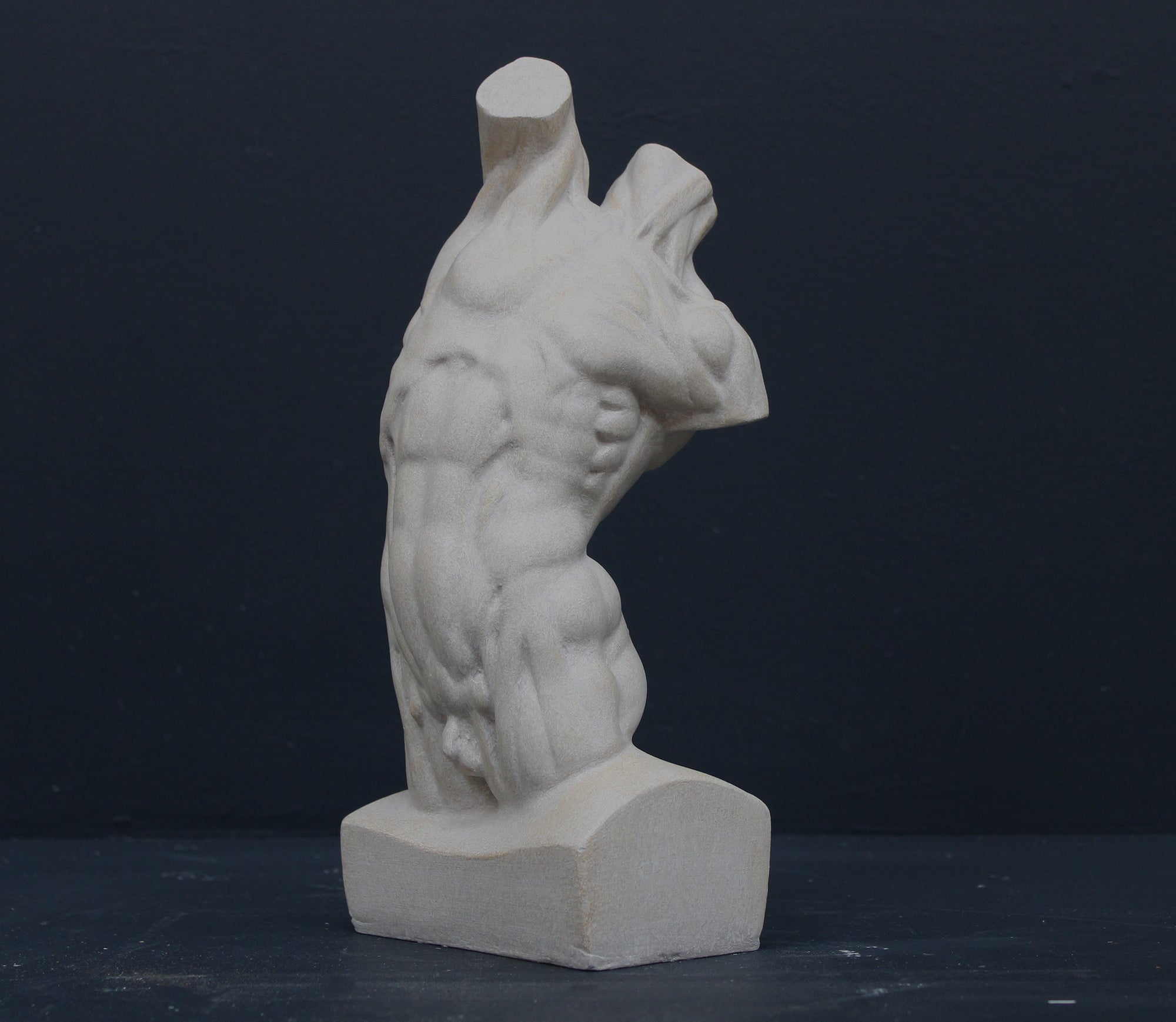 Photo of plaster cast sculpture of flayed male torso and a sculpting tool on a gray surface in front of a black background