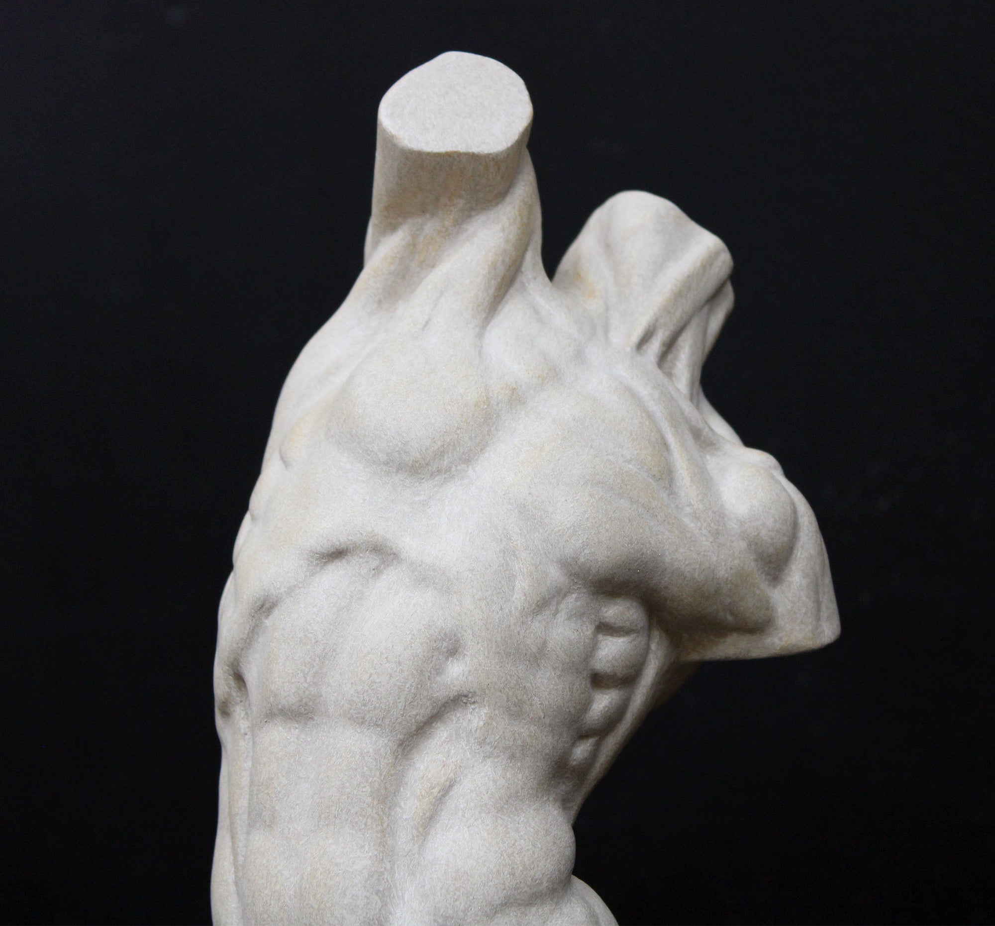 Photo of plaster cast sculpture of flayed male torso and a sculpting tool on a gray surface in front of a black background