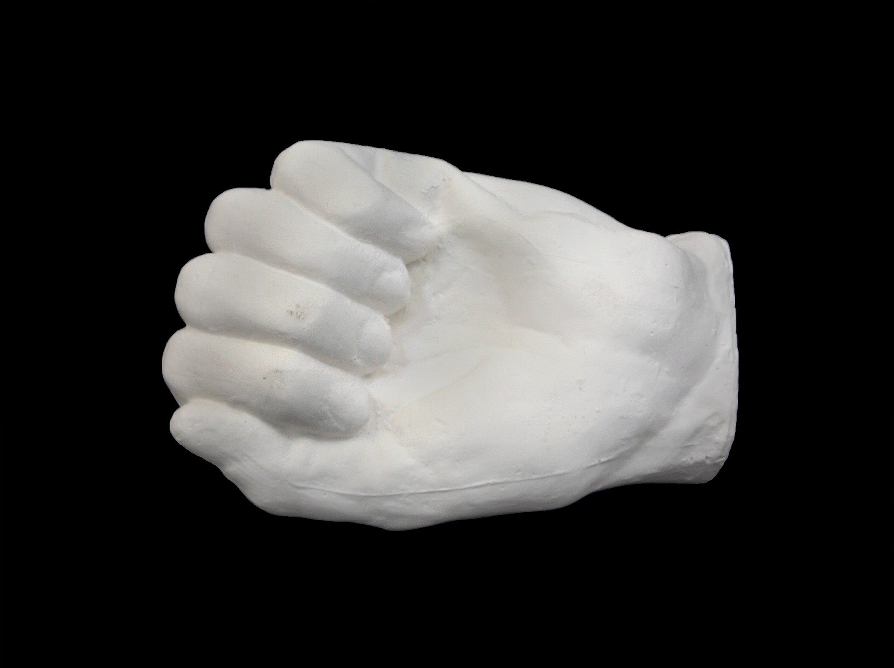 Photo of white plaster cast of a life cast of a clenched fisted hand on a black background