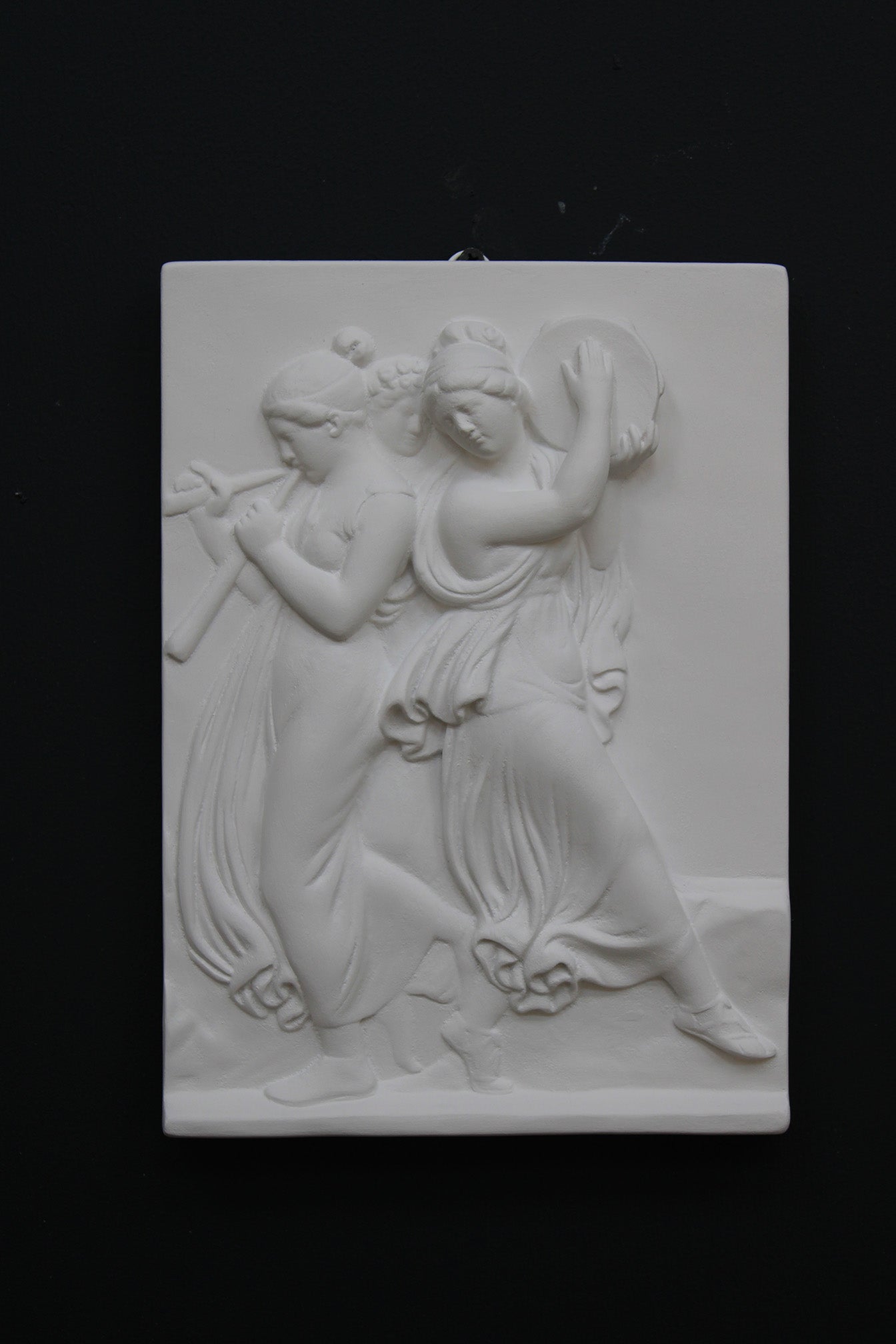 Photo with black background of plaster cast sculpture relief of females playing instruments