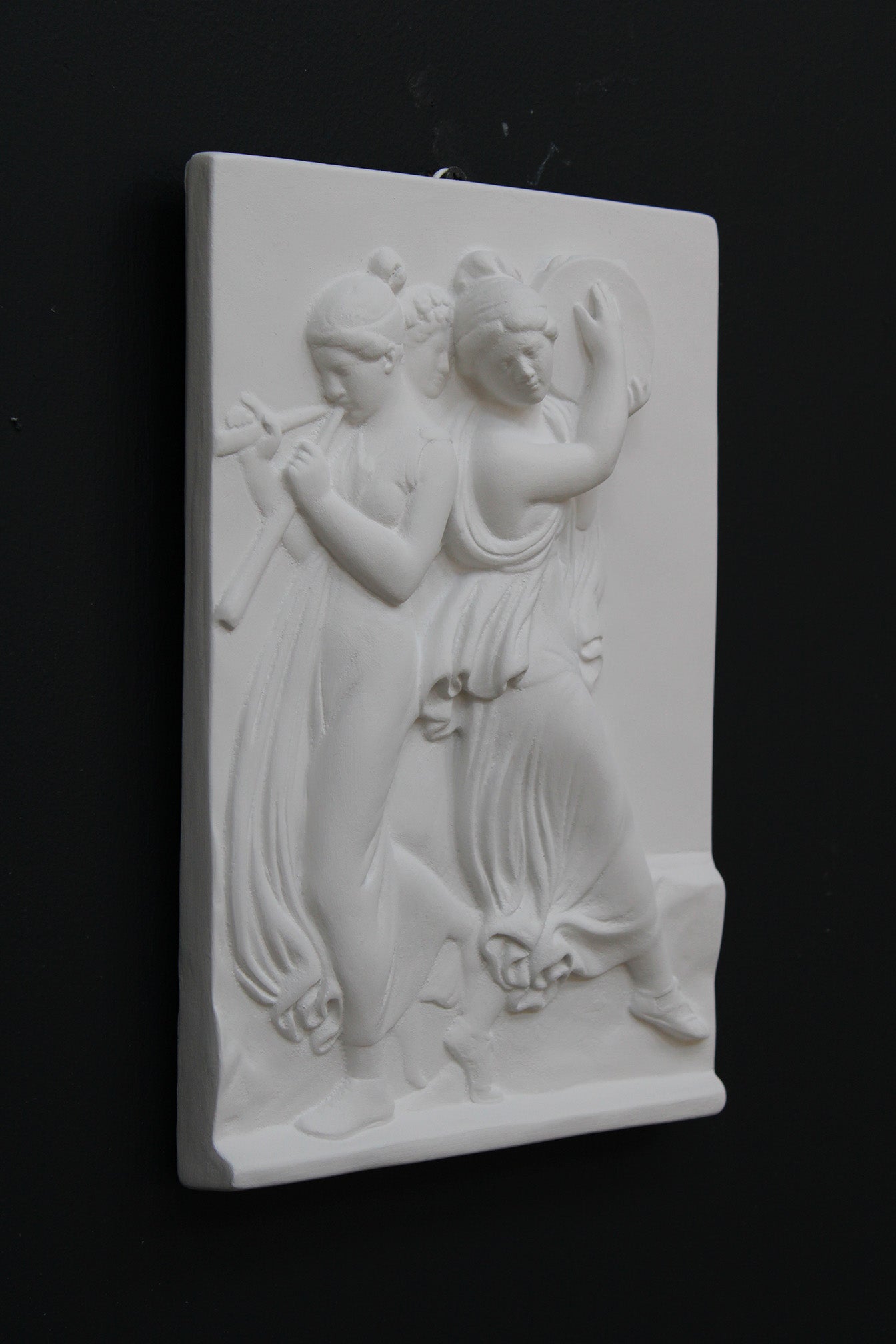 Photo with black background of plaster cast sculpture relief of females playing instruments